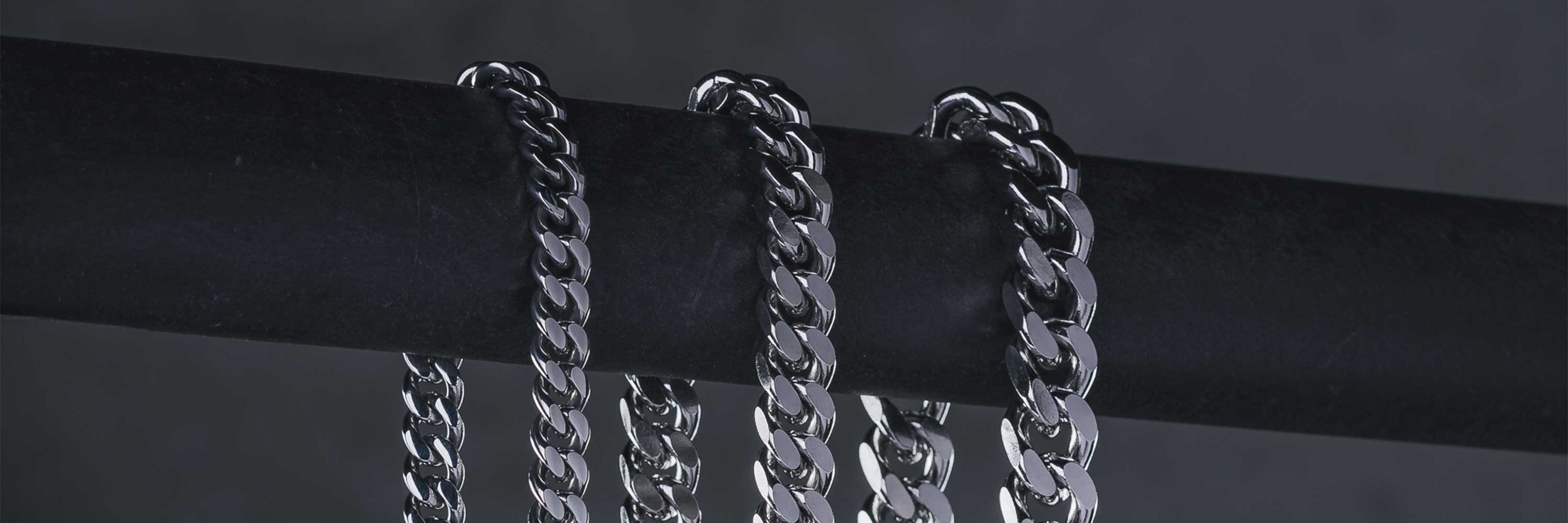 Three silver chains draped over a horizontal black rod against a dark background, showcasing their shiny, interlocking links.