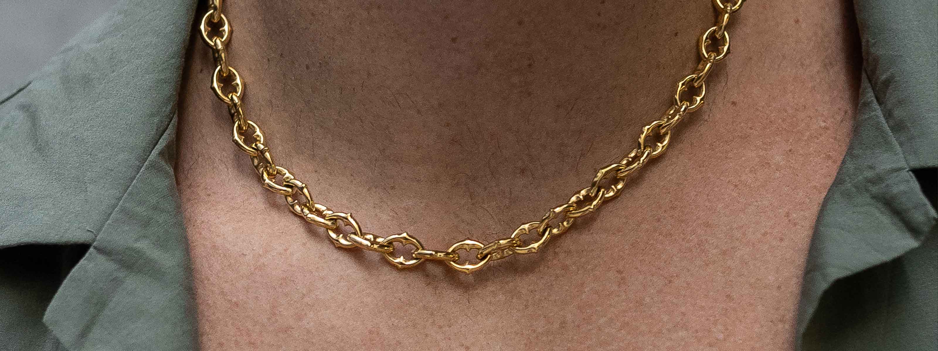 A close-up of a person wearing a gold chain necklace with twisted links, paired with a green collared shirt.