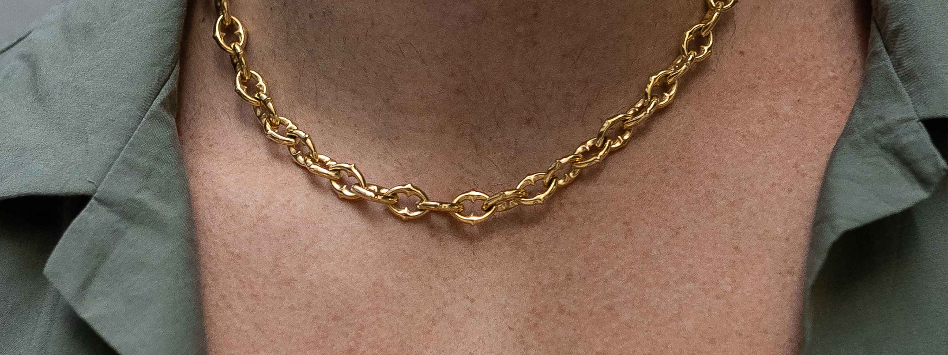 A close-up of a person wearing a gold chain necklace and a green collared shirt. The focus is on the necklace and the upper chest area.