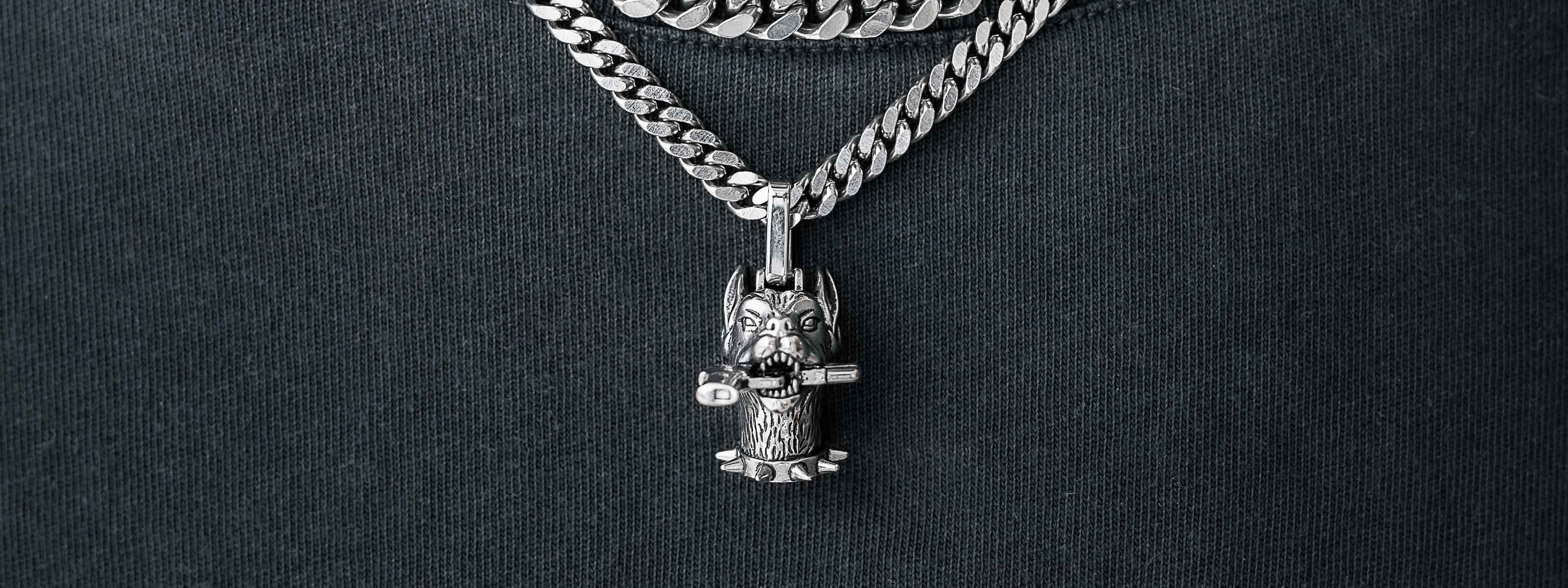 A silver chain necklace with a detailed owl-shaped pendant featuring textured wings and a small key, worn over a dark fabric background.