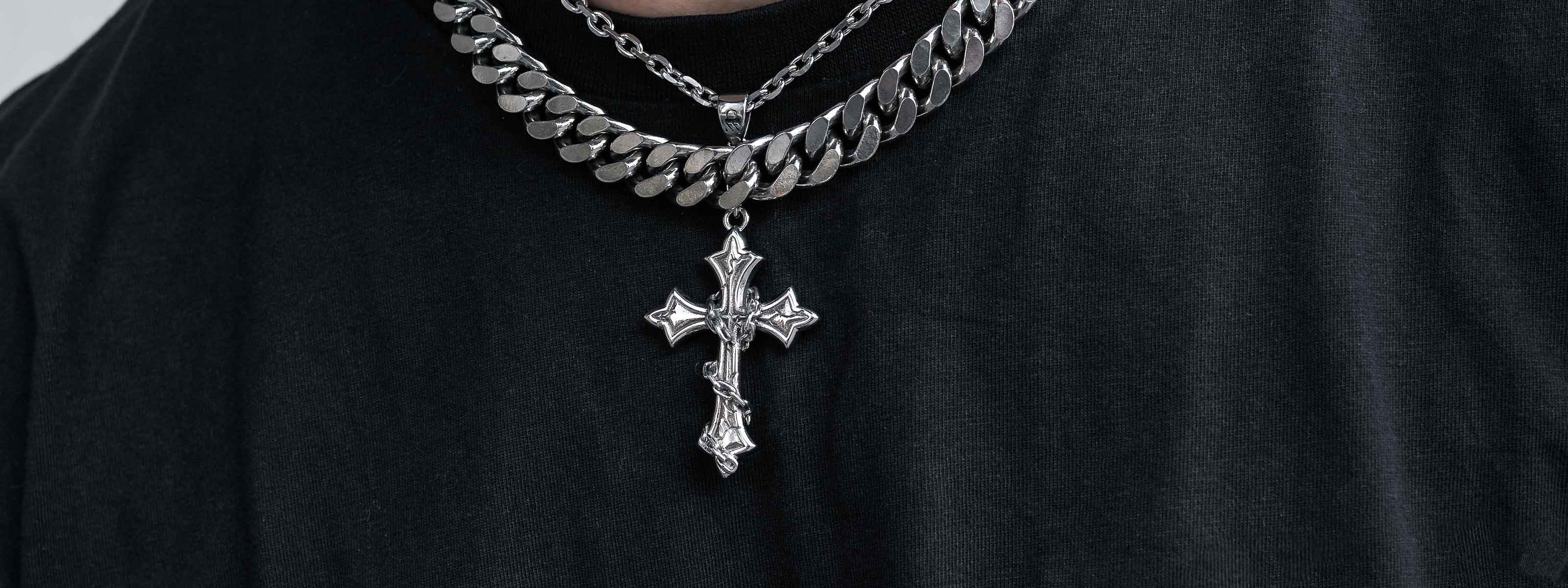 A person wearing a chunky silver chain necklace and a detailed silver cross pendant over a black shirt.
