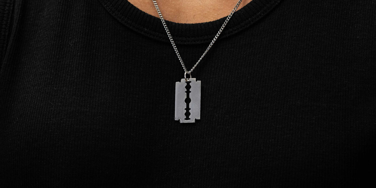 A person wearing a chunky silver chain necklace and a detailed silver cross pendant over a black shirt.