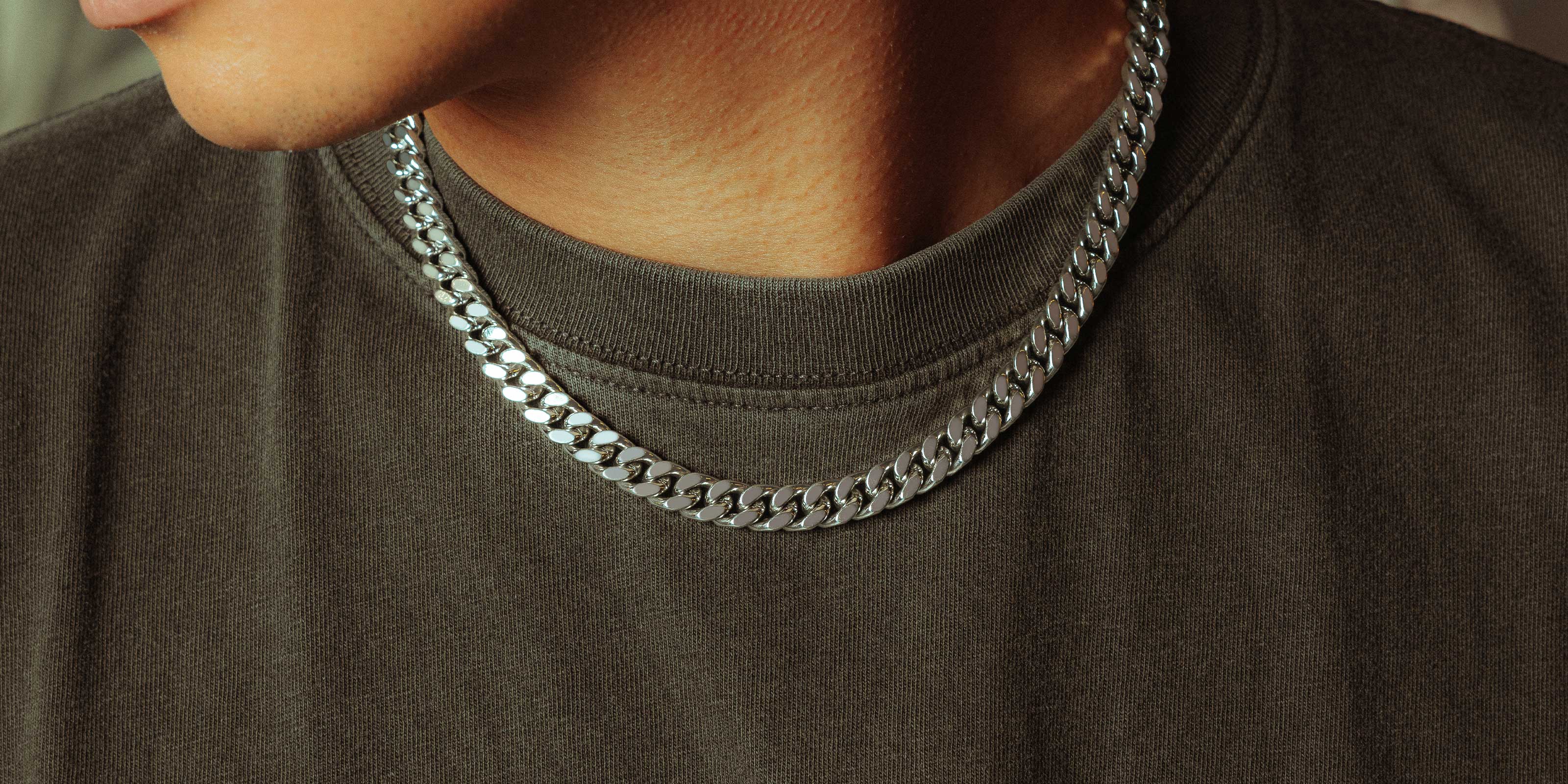 A person wearing a dark shirt and a thick silver chain necklace. Only the lower half of the face and the neck are visible.