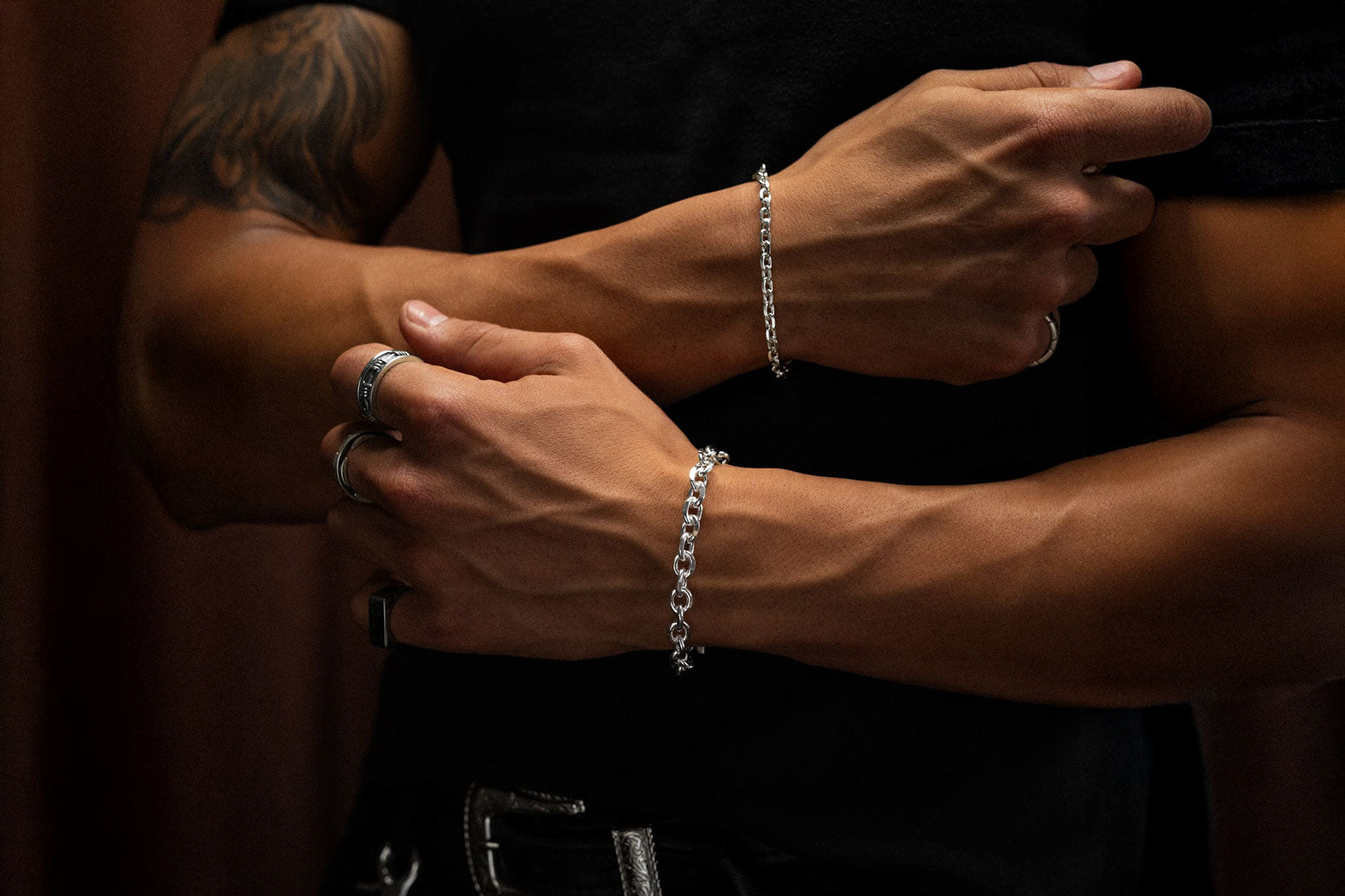 man with black shirt wearing bright sterling silver bracelets by statement collective against brown background