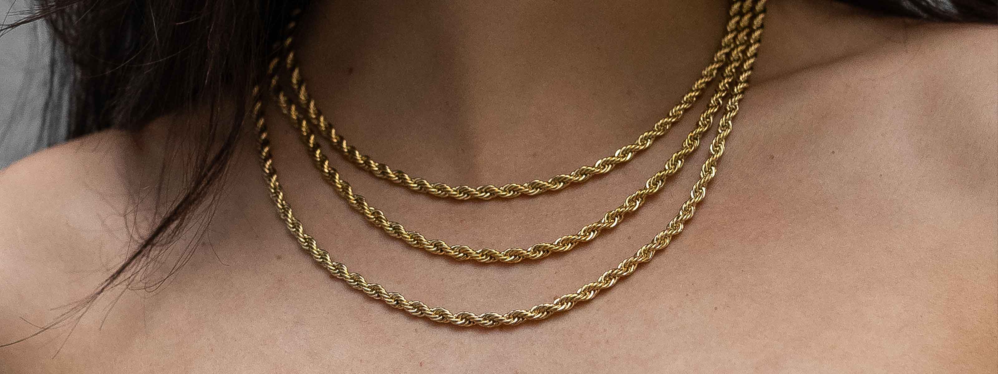 A person wearing three layered gold rope chain necklaces against bare skin, with dark hair partially visible on the left side.