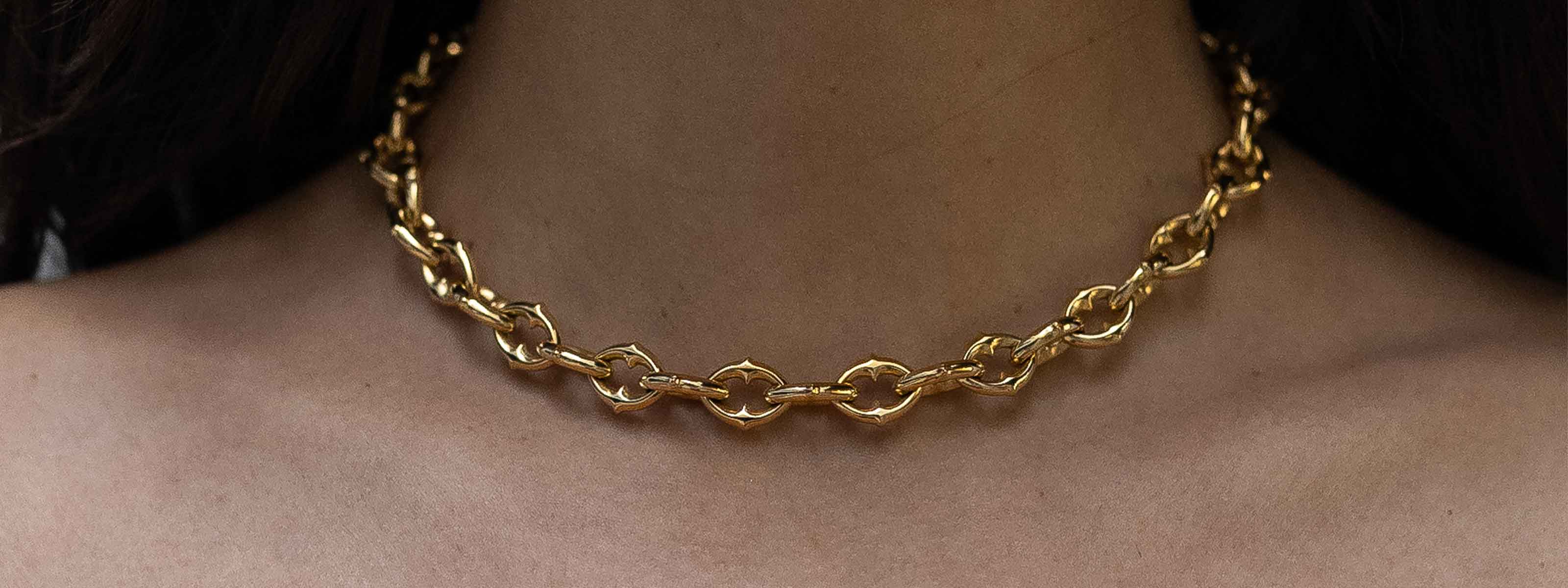 Close-up of a person wearing a chunky gold chain necklace with interlocking links, shown against bare skin at the neck and shoulders.