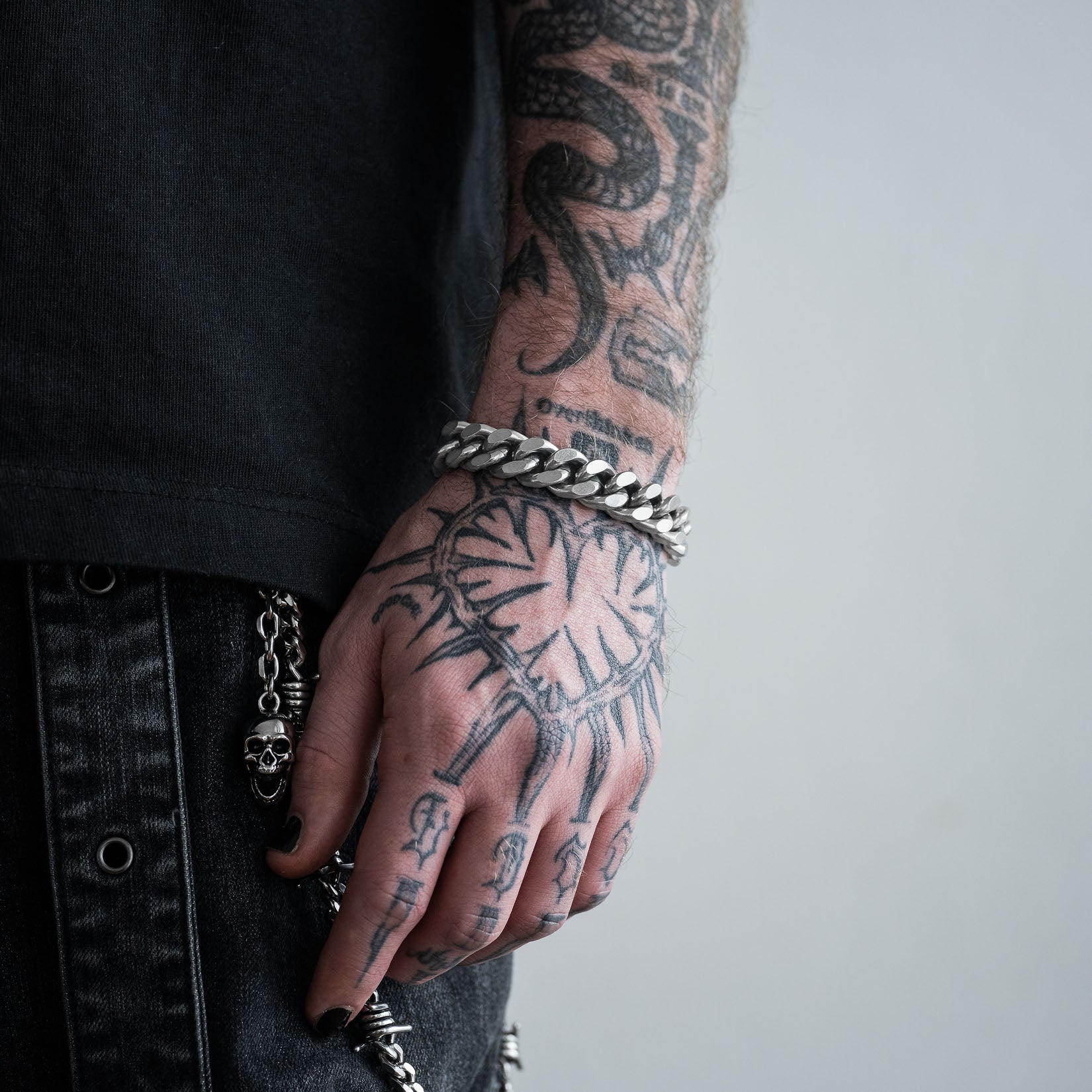 Tattooed hand with silver 13mm cuban chain bracelet on a plain background