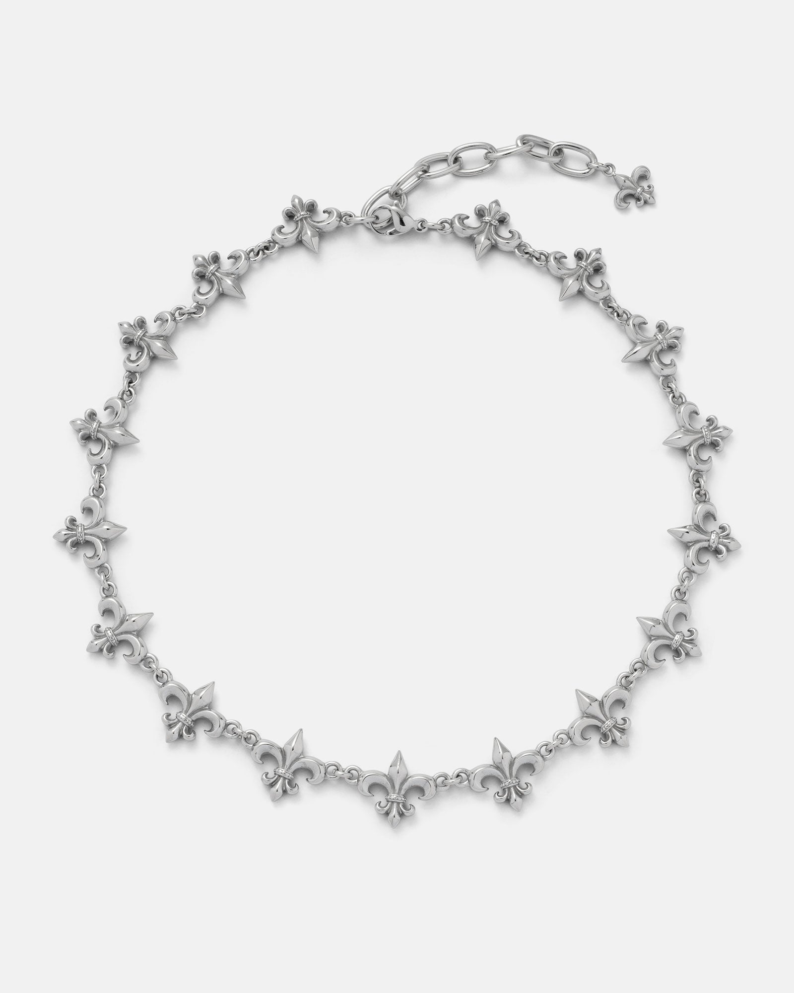 The "Fleur De Lis" 15mm Chain by Statement Collective features linked fleur-de-lis charms evenly spaced along a silver chain, with an adjustable clasp and a dangling charm at the end, displayed on a plain white background.