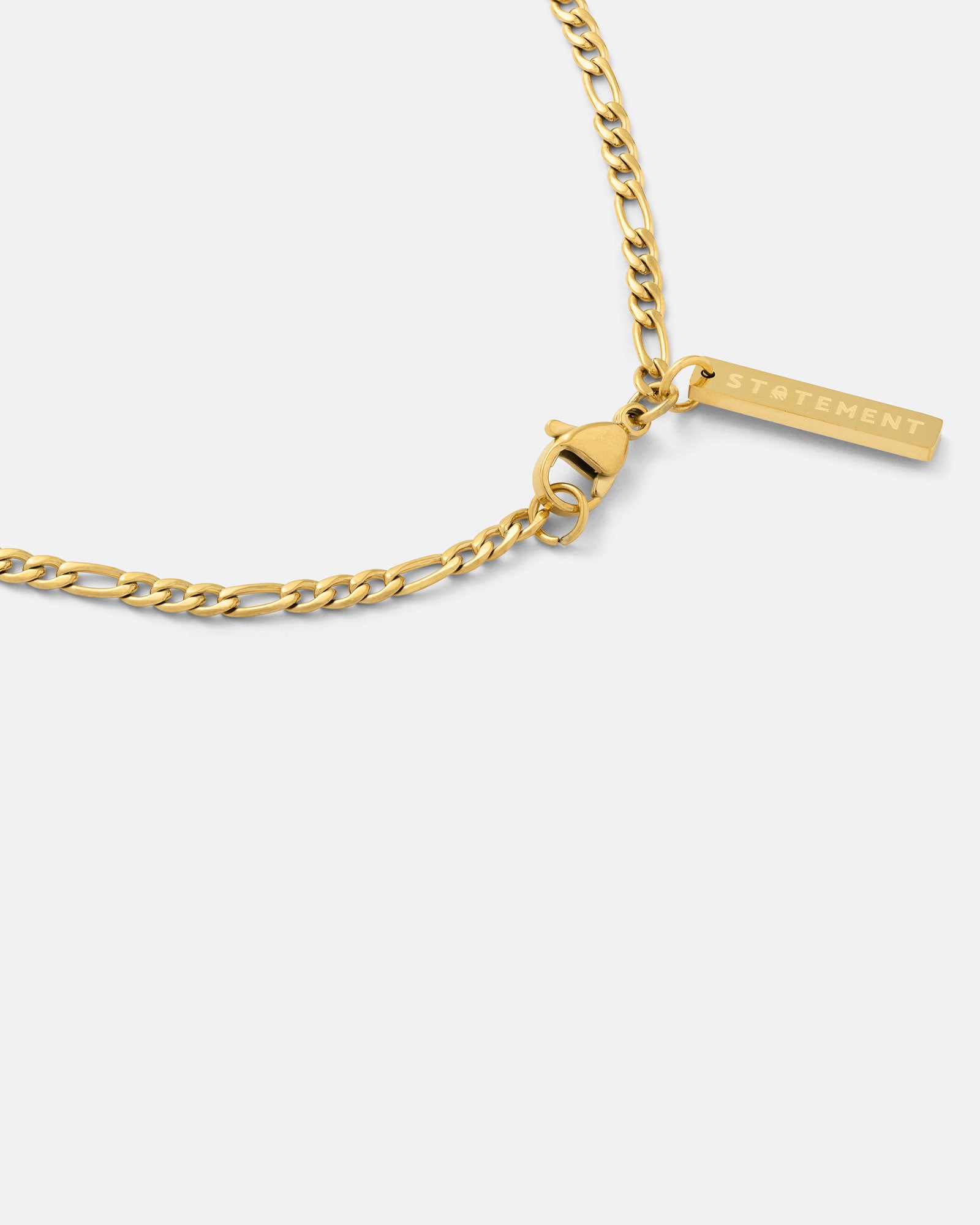 A 2.9mm Figaro Chain (Gold) necklace with a rectangular STATEMENT-engraved pendant near the lobster clasp, shown on a white background.