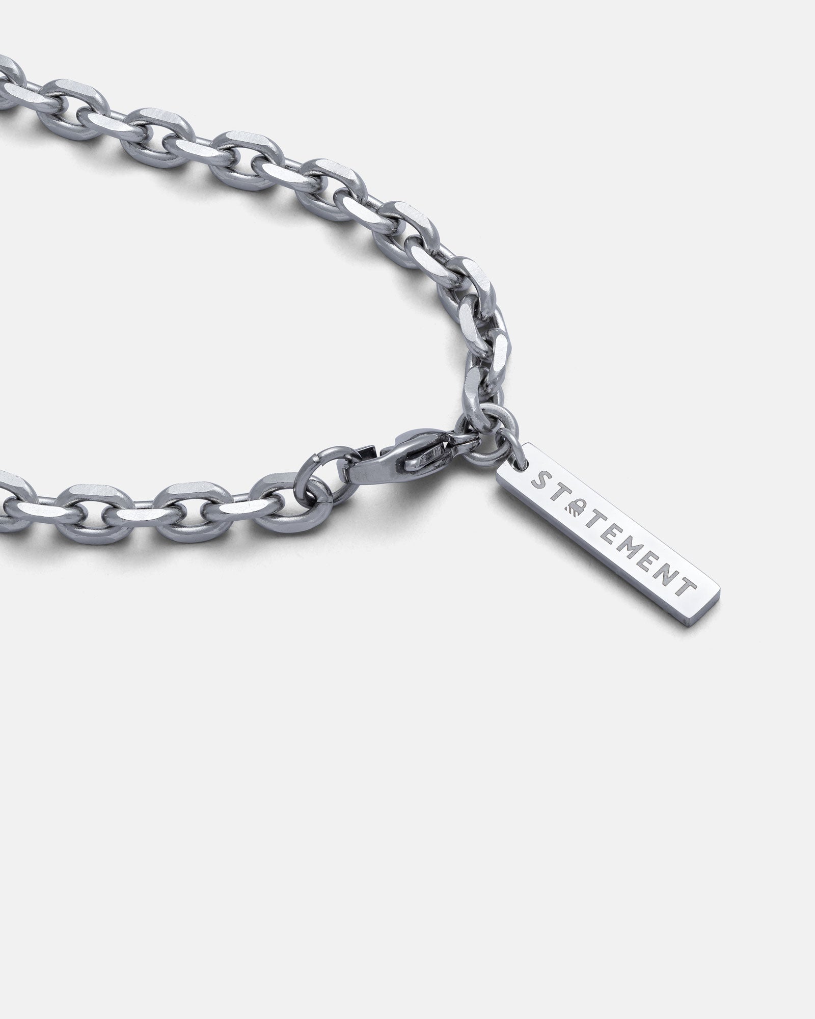 The 4.5mm Cable Chain, a stainless steel necklace with a rectangular pendant engraved STATEMENT, is displayed on a white background. Its beveled cable link and diamond-cut edges add shine and elegance to this striking accessory.