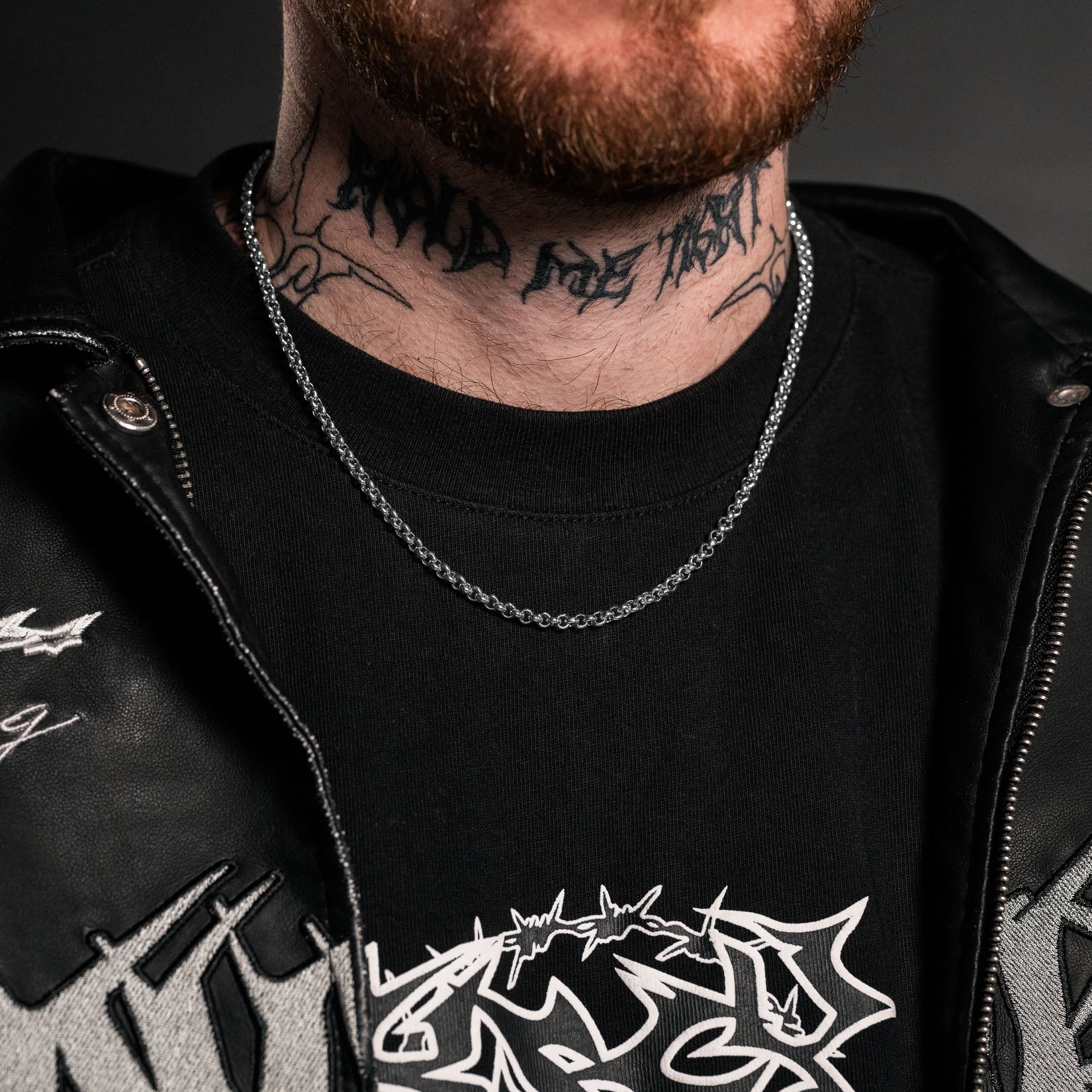 Person wearing a black jacket with white designs and a black shirt with white graphics, featuring tattoos on the neck.