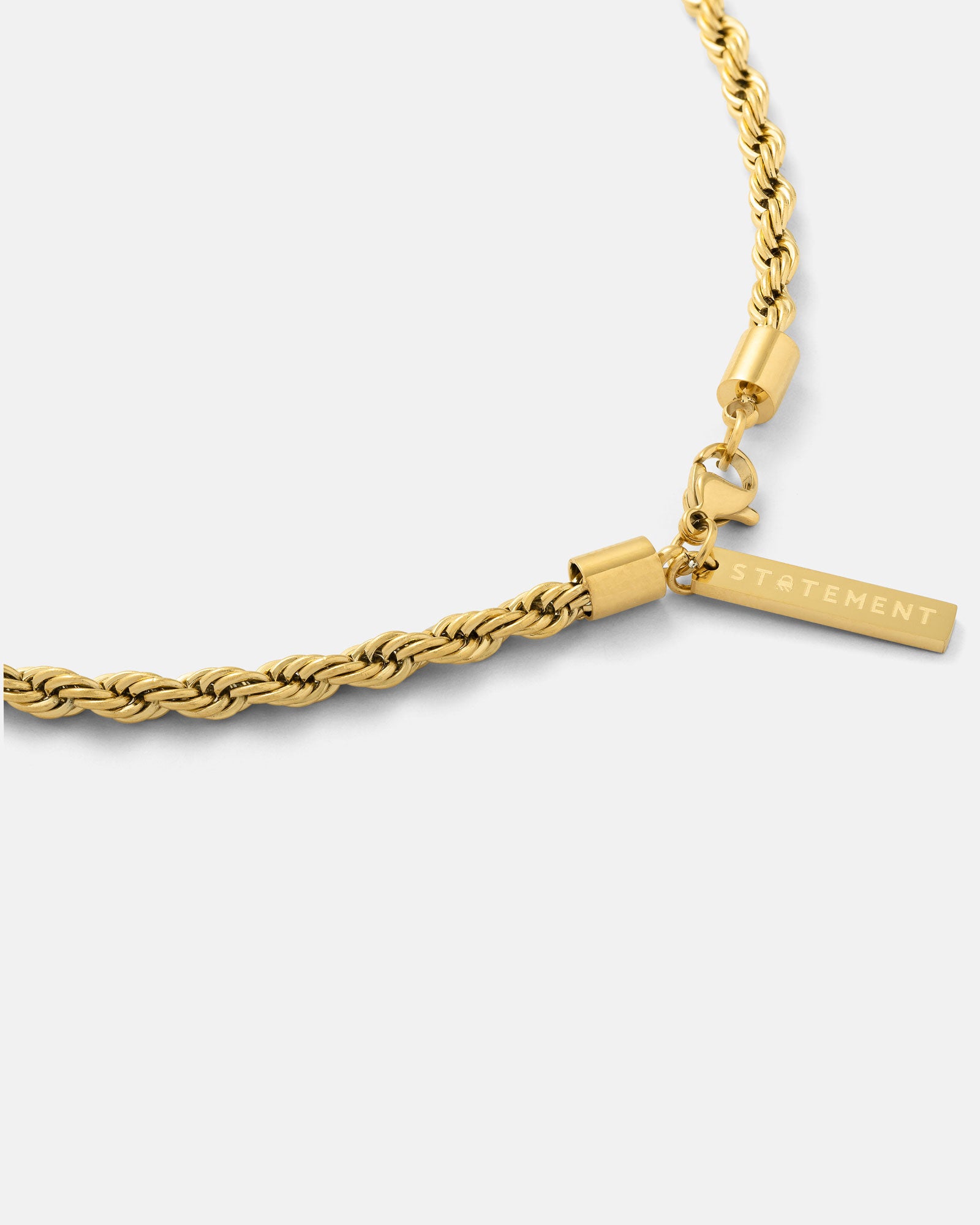 A close-up of the 4mm Rope Chain (Gold) features a gold rope chain necklace with a rectangular pendant engraved "STATEMENT," made from durable stainless steel and set against a plain light background.