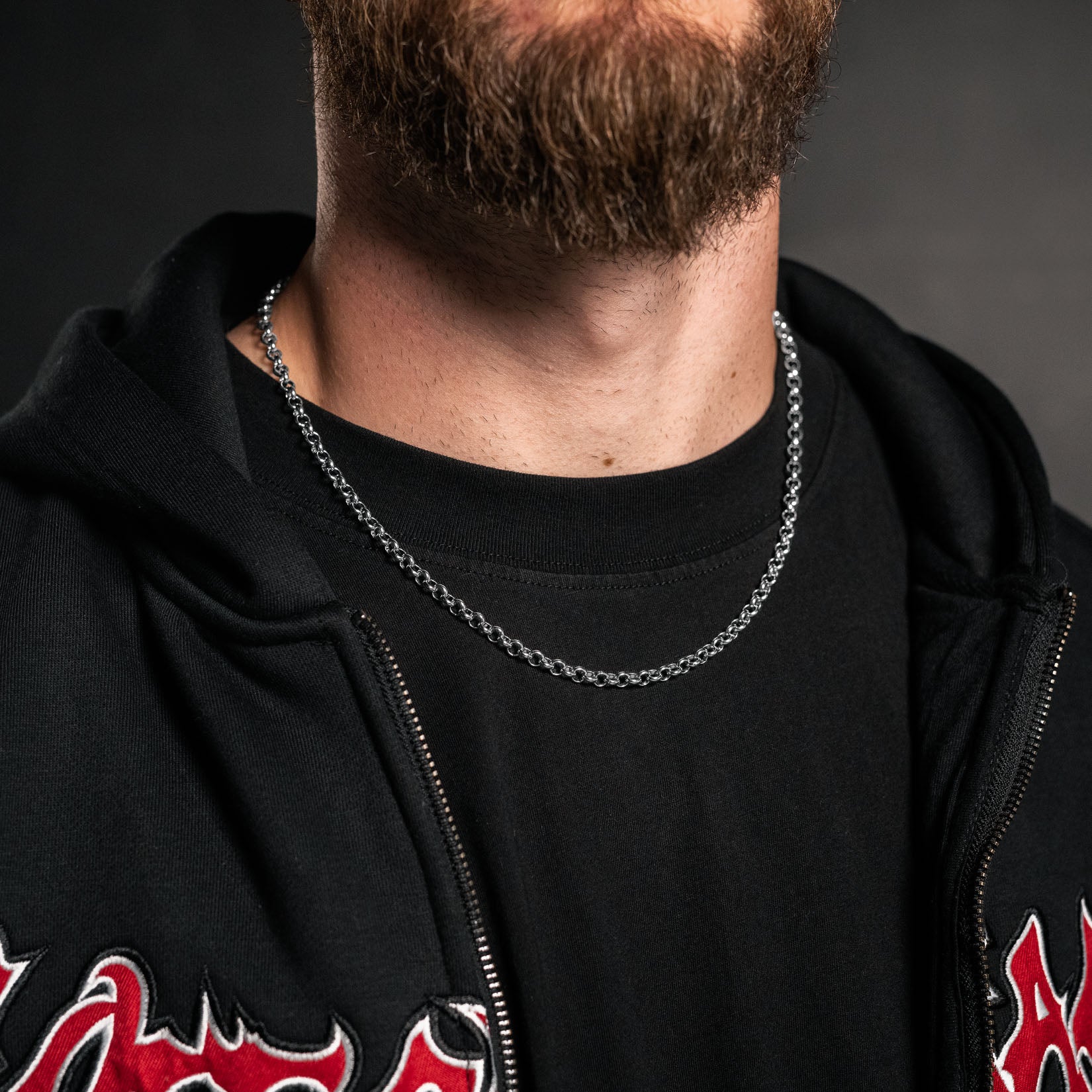 Person wearing a black hoodie with red designs and a silver chain necklace against a dark background