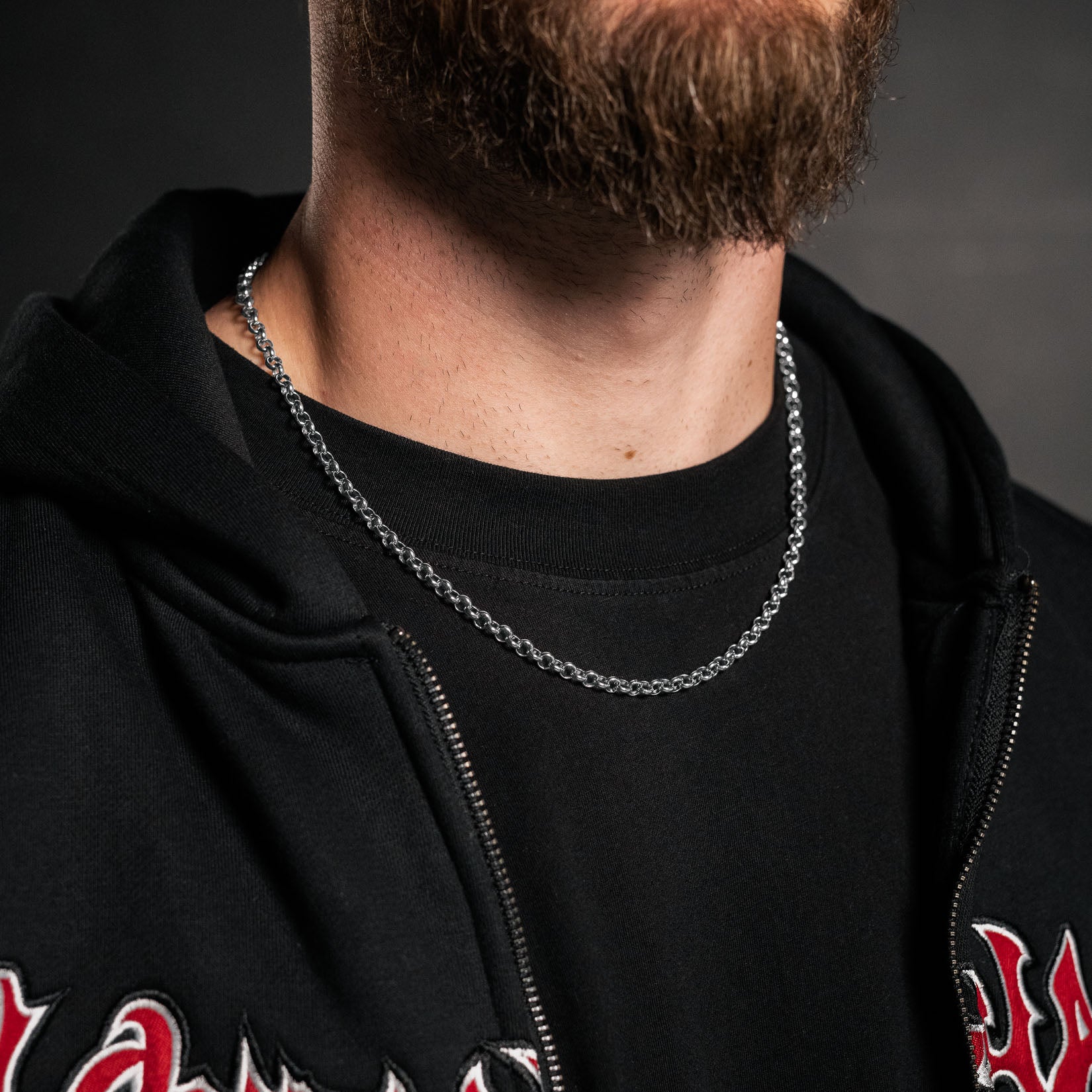 man with silver rolo chain necklace wearing hoodie on dark background by statement collective
