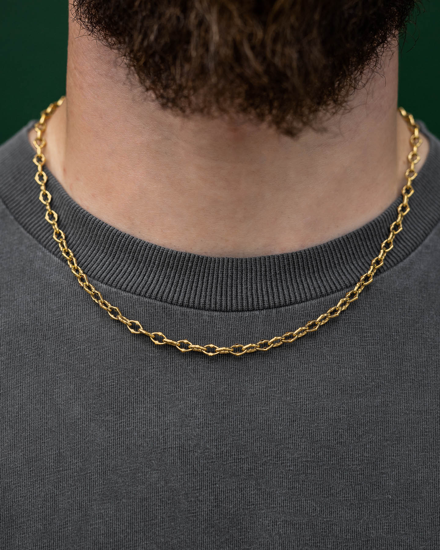 A close-up of a person wearing "The Cathedral" 6mm Spiked Chain (Gold) over a dark gray crew-neck shirt, with the focus on the neck and part of a beard visible at the top.
