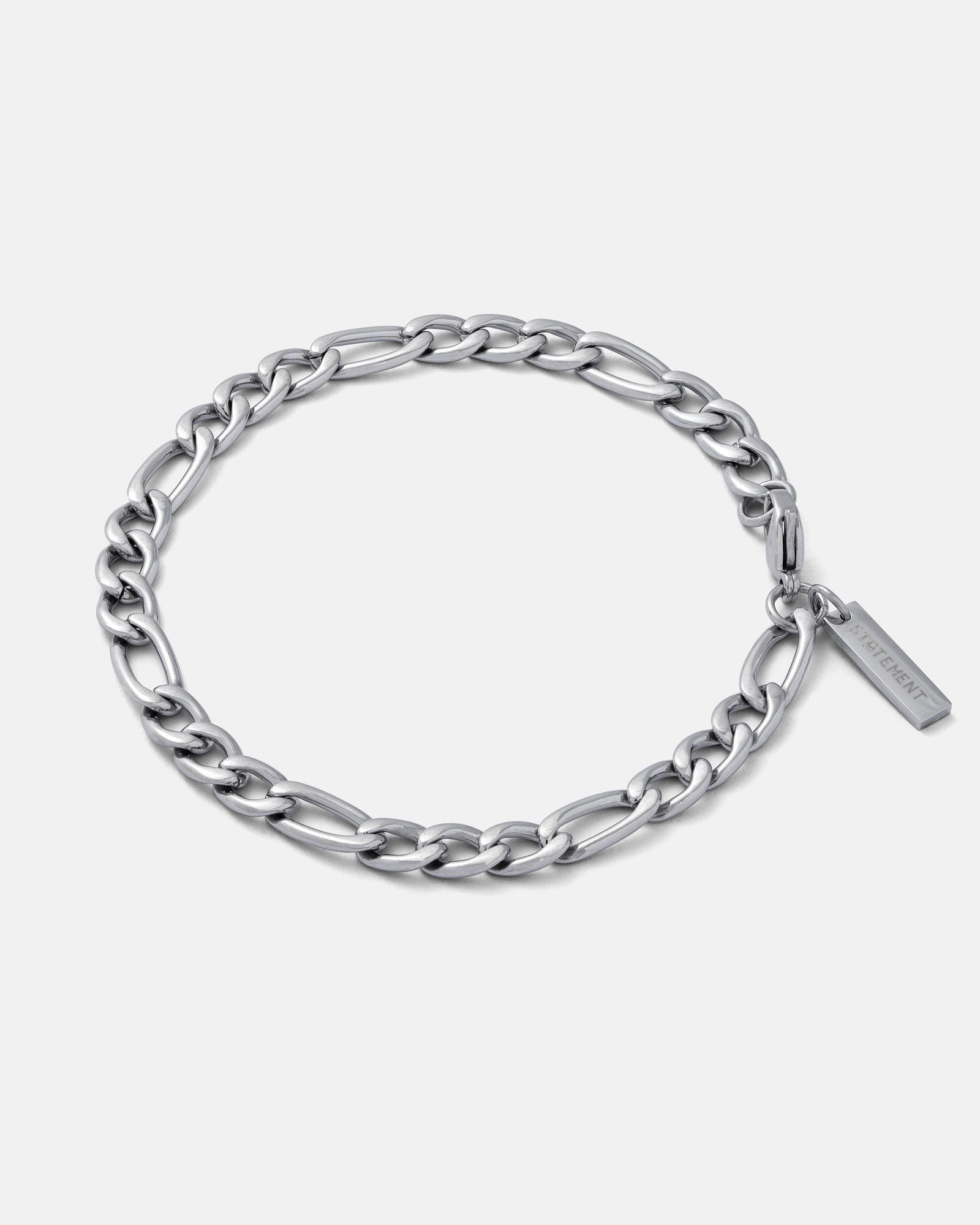 silver 6mm figaro style chain bracelet with branded tag on the clasp by statement collective on grey background.
