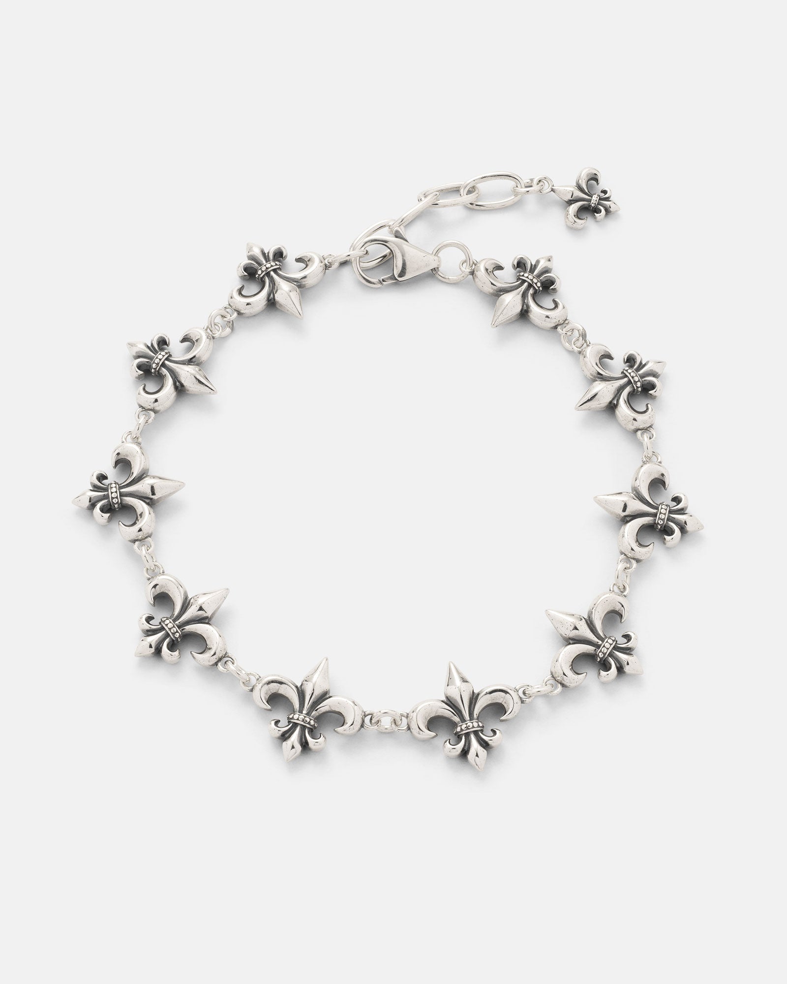 The Statement Collective 925 Sterling Silver "Fleur De Lis" 15mm Bracelet showcases multiple intricately crafted fleur-de-lis charms linked together, complete with an adjustable lobster clasp closure and a delicate additional fleur-de-lis charm at the end.