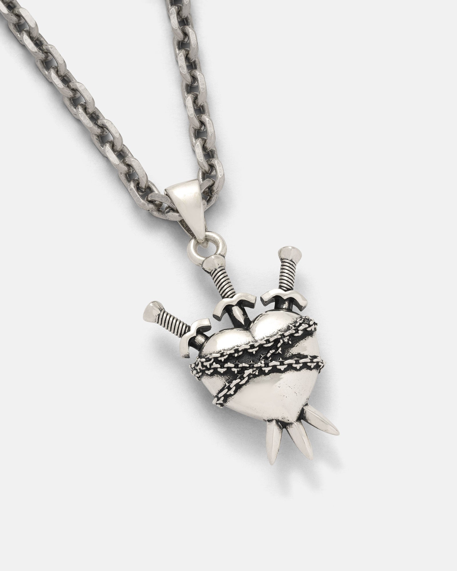 The 925 Sterling Silver "3 of Swords" Pendant features a heart wrapped in barbed wire and pierced by three swords, hanging from a thick chain and displayed against a plain light background.