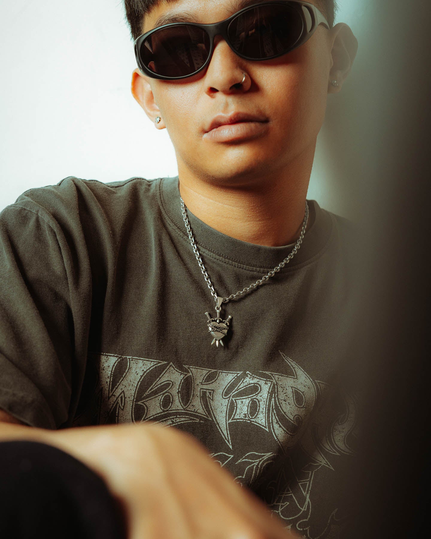 A person wearing dark sunglasses, a dark graphic tee, and a tarot chain necklace with a 925 Sterling Silver "3 of Swords" Pendant sits against a light background, looking at the camera.