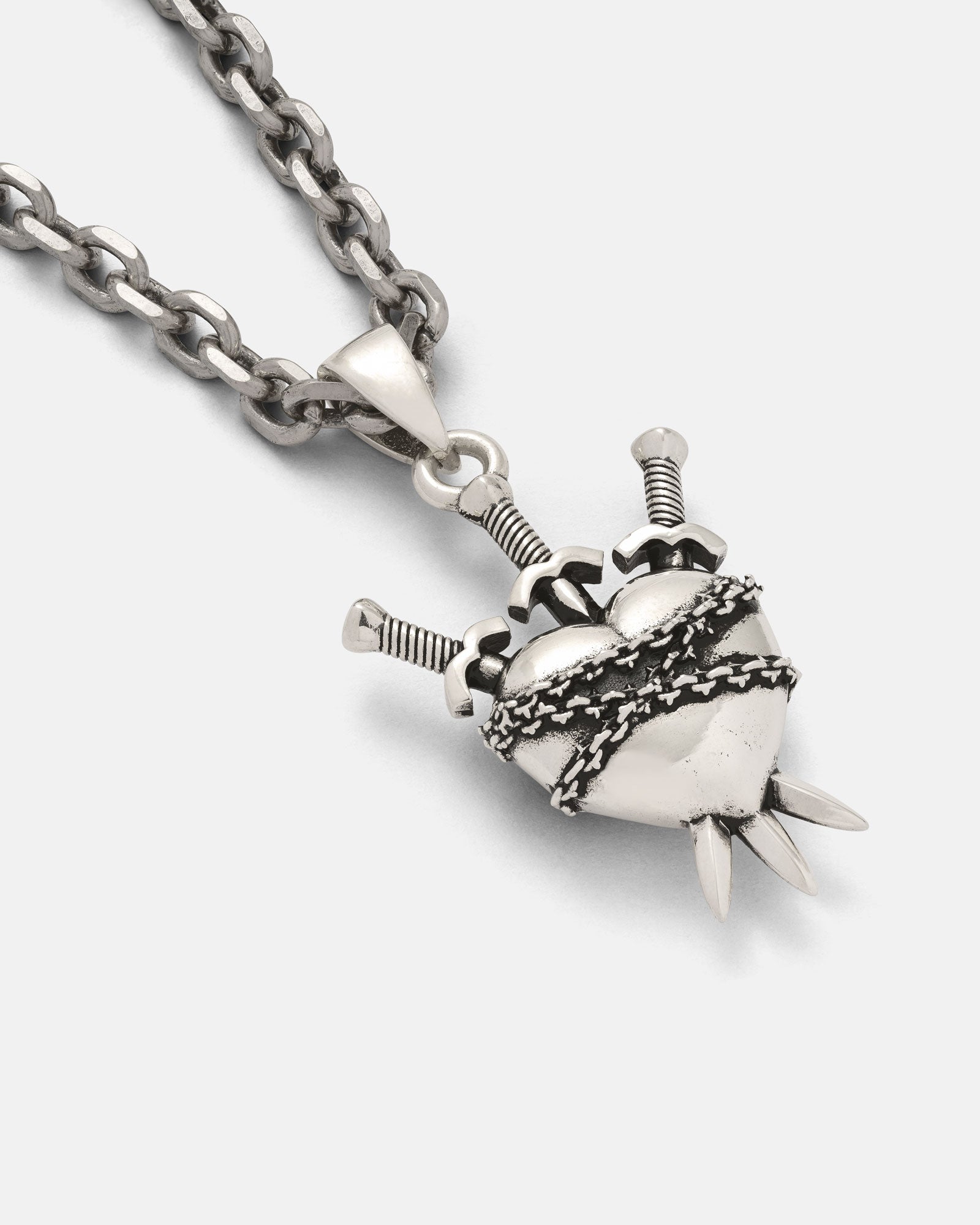 The 925 Sterling Silver "3 of Swords" Pendant, shaped like a heart wrapped in barbed wire pierced by three swords, hangs from a thick chain necklace against a white background.