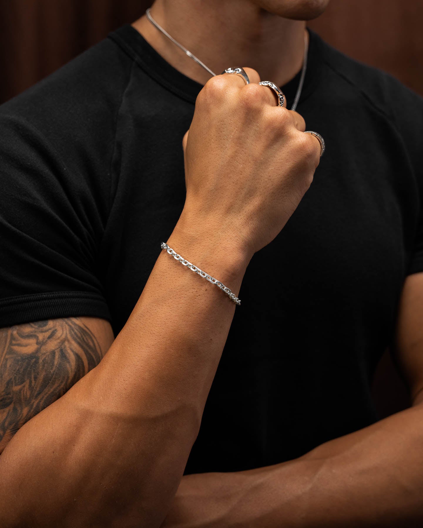 male model in tight black compression top holding first up to show the 4.5mm cable bracelet in sterling silver around his wrist.