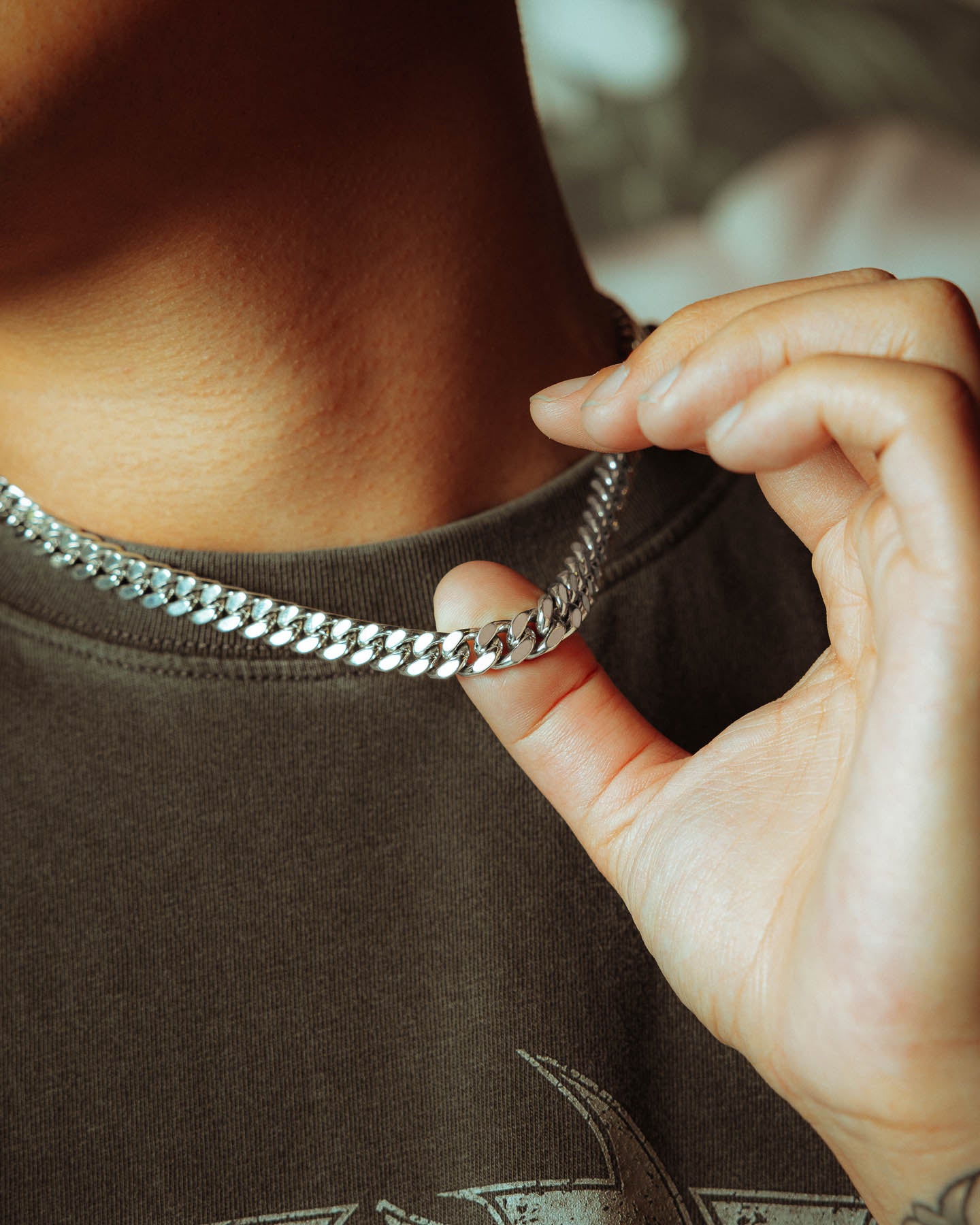 A close-up of a person in a dark shirt holding the 925 Sterling Silver 9mm Cuban Chain near their neck with their right hand.