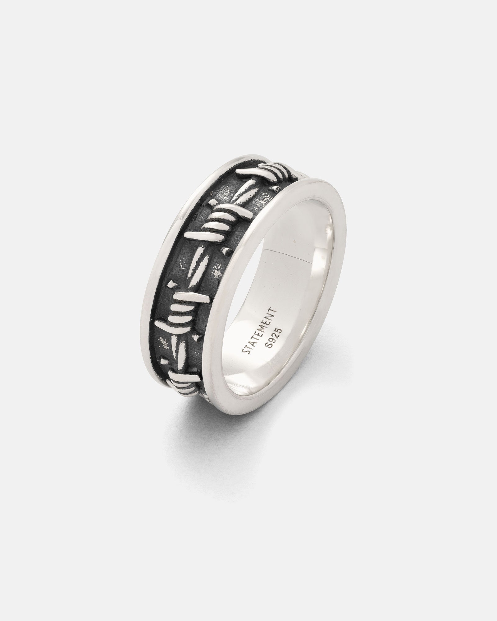 The 925 Sterling Silver Barbed Wire Ring features a dark, oxidized center with a raised intertwined barbed wire design and a smooth inner band engraved with "STATEMENT 925.