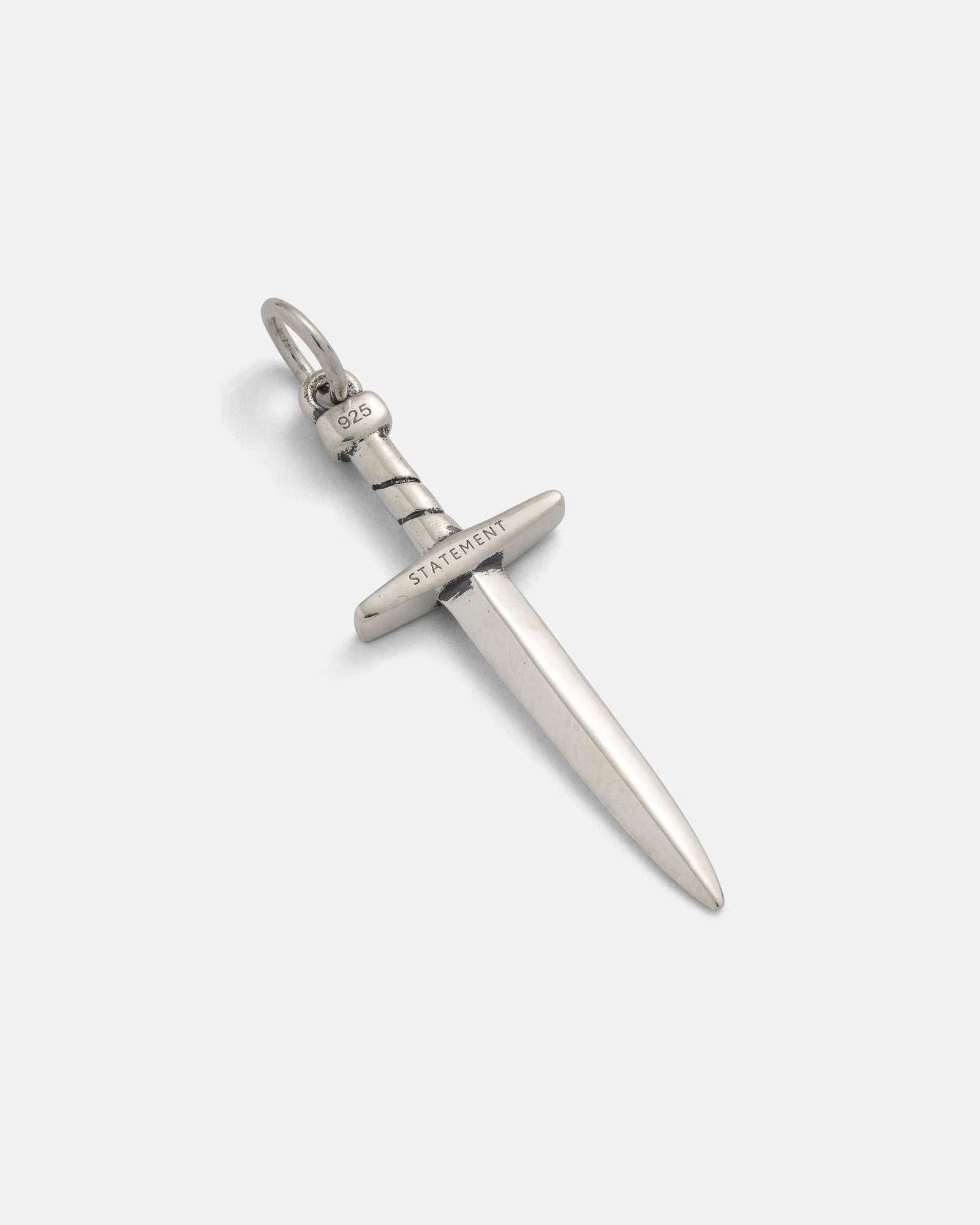 925 Sterling Silver Dagger Pendant by Statement Collective, crafted in a sword-shaped, handmade design with a loop for hanging. The crossguard is engraved with “STATEMENT,” and “925” is stamped on the hilt. Displayed against a plain white background, this unique pendant showcases expert craftsmanship and bold style in .925 sterling silver.