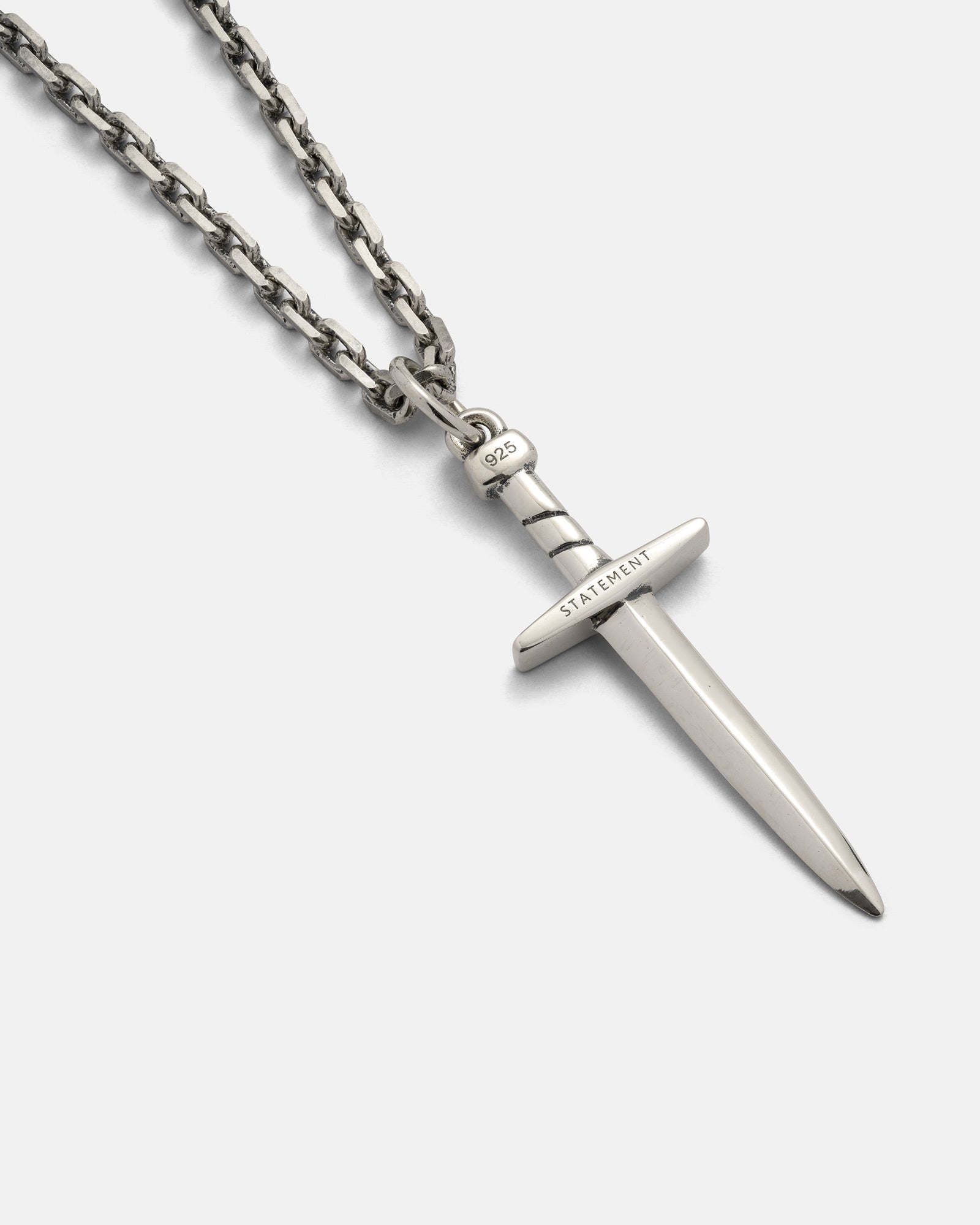 The 925 Sterling Silver Dagger Pendant by Statement Collective is showcased on a light background. This eye-catching necklace features a silver chain and a handmade dagger pendant, with "STATEMENT" engraved on the hilt and "925" on the handle. Expertly crafted from .925 sterling silver, it offers both style and lasting quality.