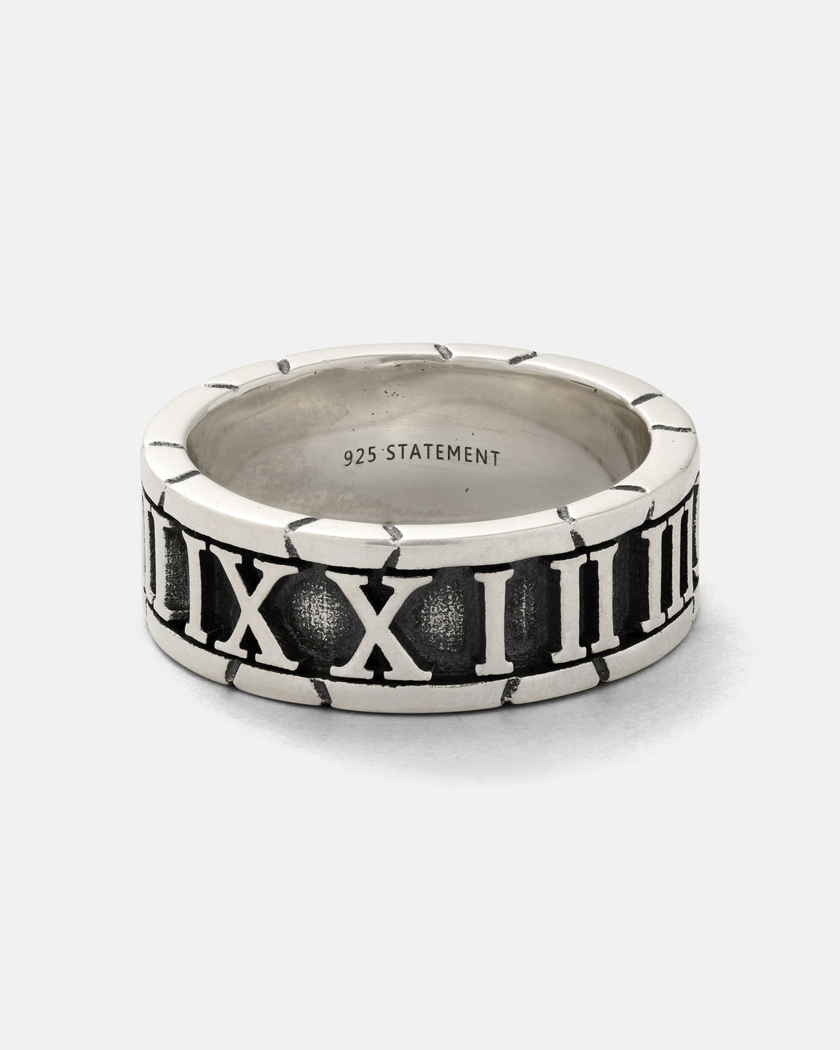 Introducing the 925 Sterling Silver Numerals Ring by Statement Collective—a handmade piece featuring engraved, raised Roman numerals encircling the band. The standout numerals are set against a dark, textured background for striking contrast, while “925 STATEMENT” is stamped on the inside. This ring blends rustic elegance with timeless detail, making it ideal for those who value artisanal craftsmanship in their jewelry.