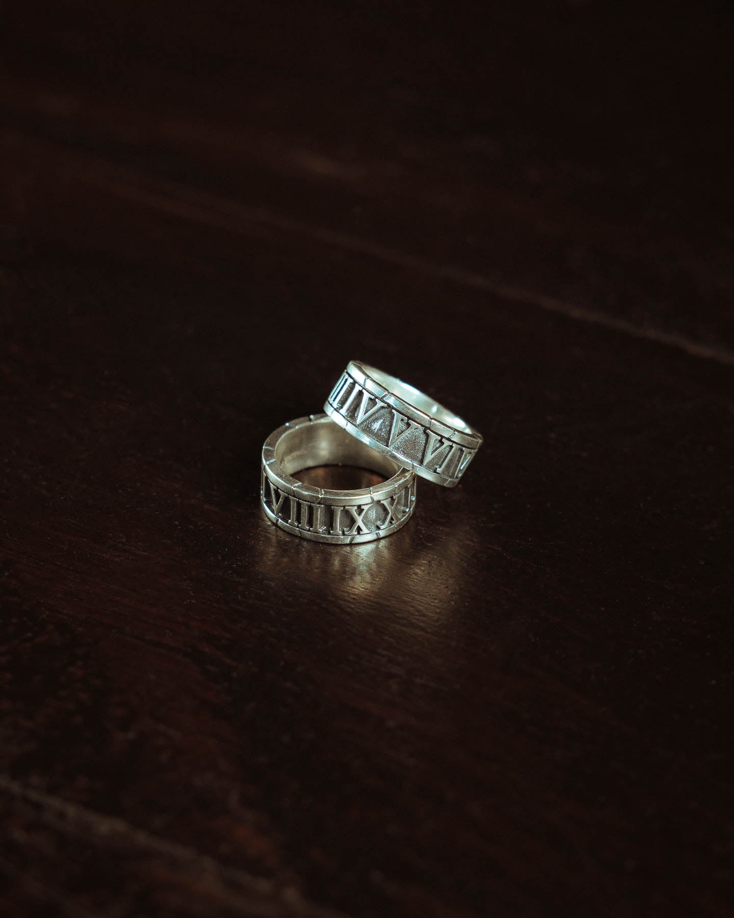 Two 925 Sterling Silver Numerals Rings rest on a dark wooden surface, highlighting timeless style and the beauty of handcrafted jewelry.
