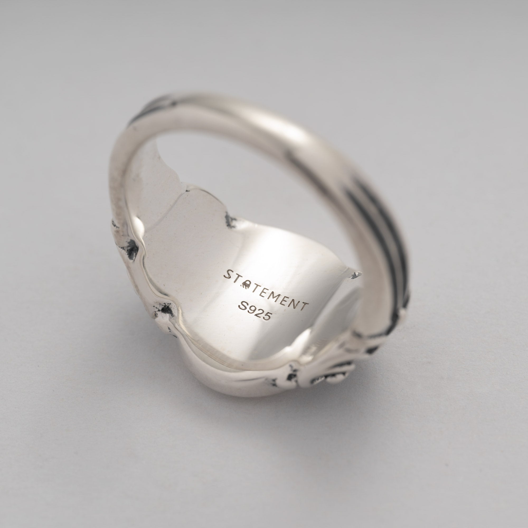 Silver ring with 'STATEMENT S925' engraving on a light gray background