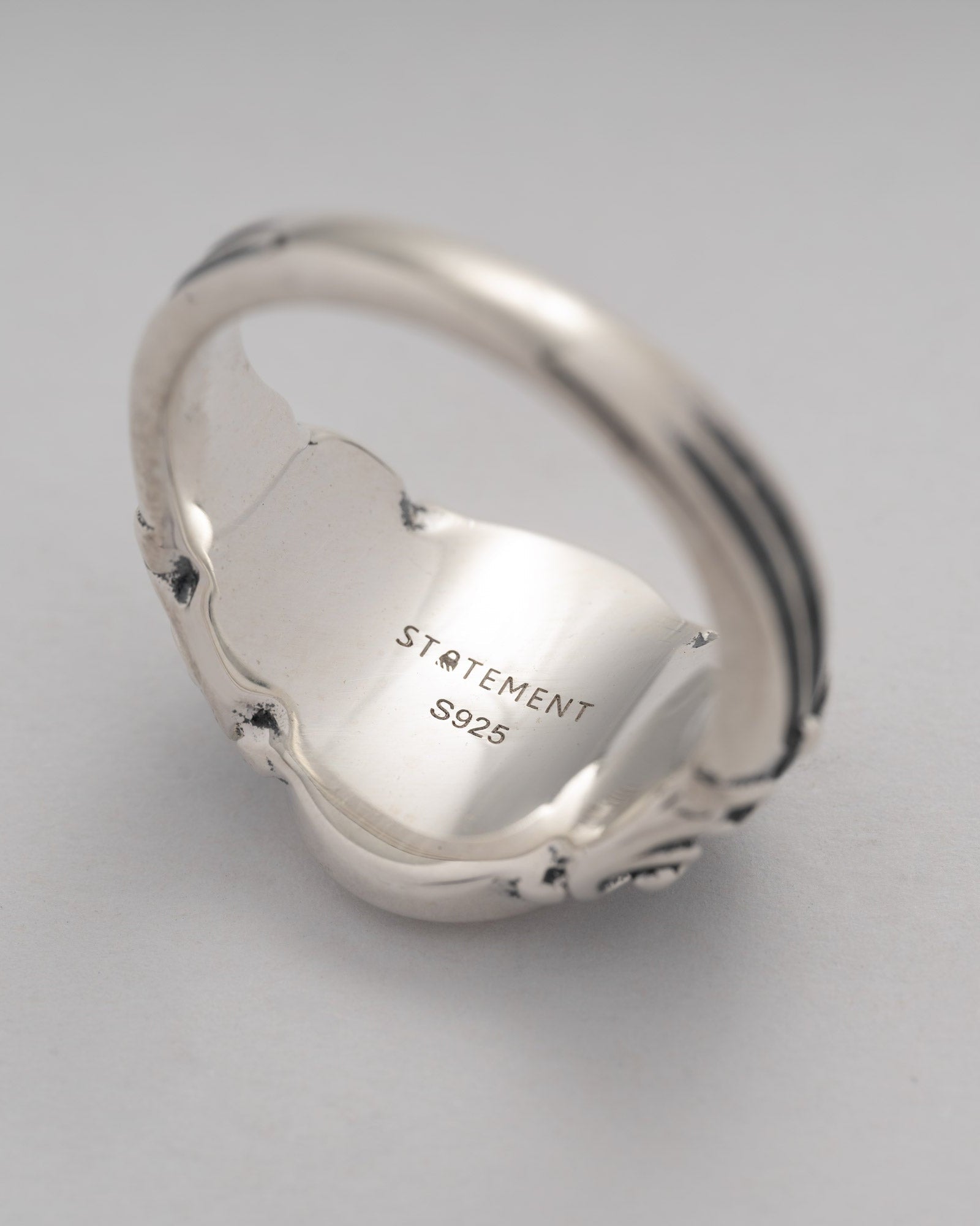 Silver ring with 'STATEMENT S925' engraving on a light gray background