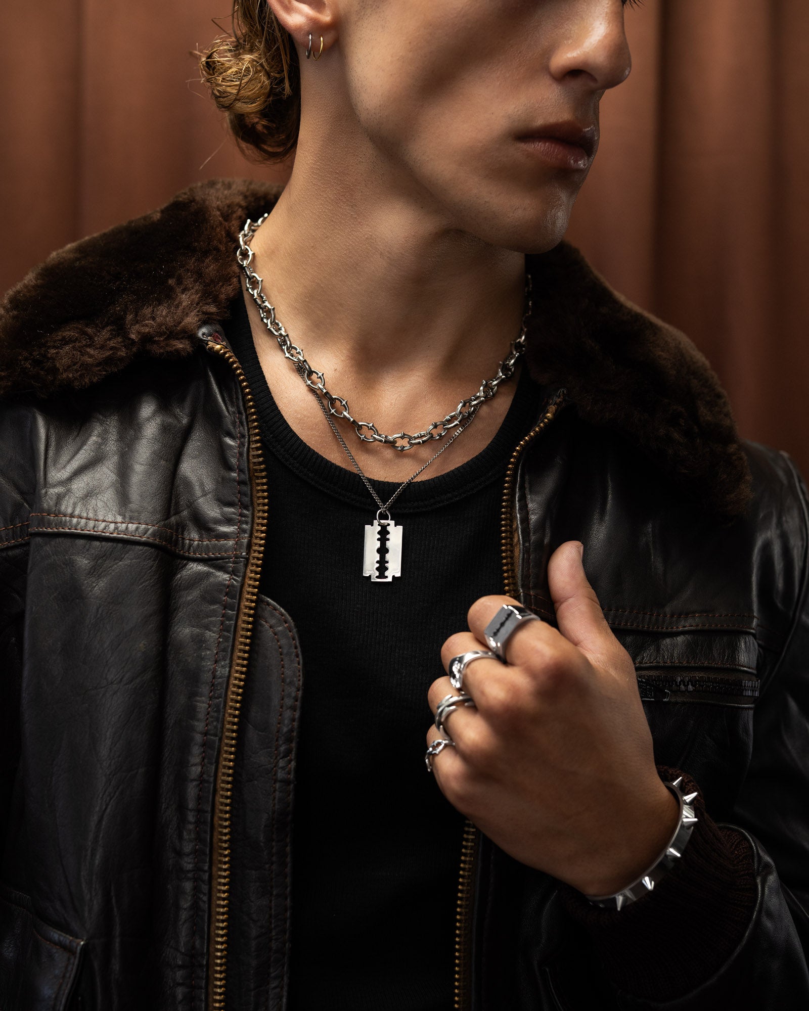 Man wearing a black leather jacket with jewelry including a razorblade necklace, ring, and bracelet in sterling silver