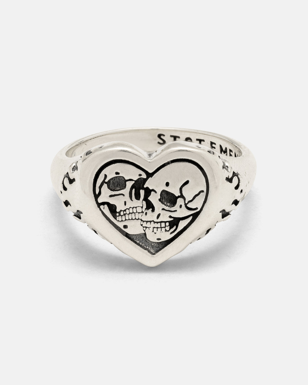 The 925 Sterling Silver Skull Heart Ring by Statement Collective showcases two skulls facing one another within a heart-shaped frame, enhanced by engraved details along the band—this handcrafted piece of silver jewelry combines edgy style with intricate artistry.