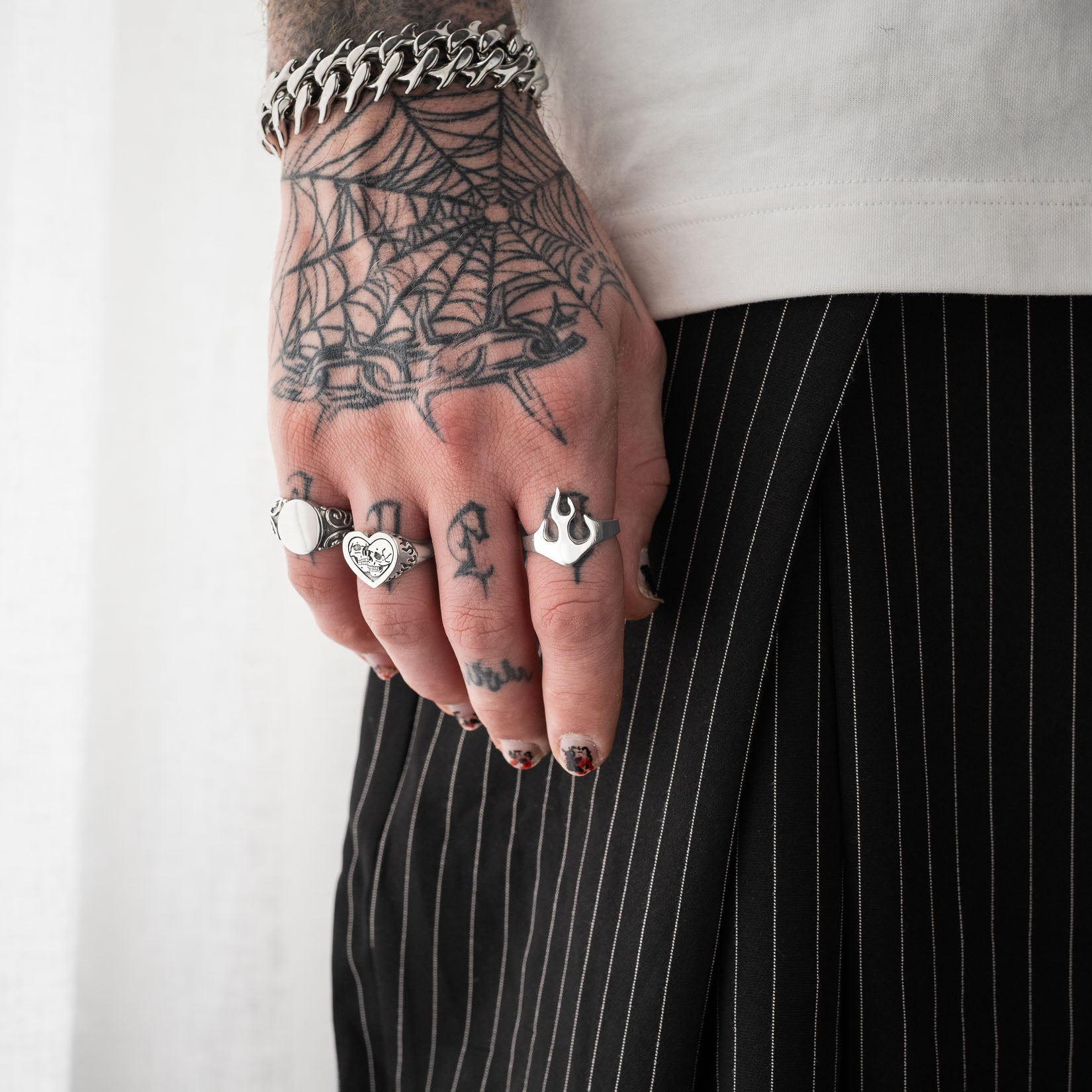 Hand with tattoos wearing a sterling silver flame ring, white shirt and black pinstripe pants.