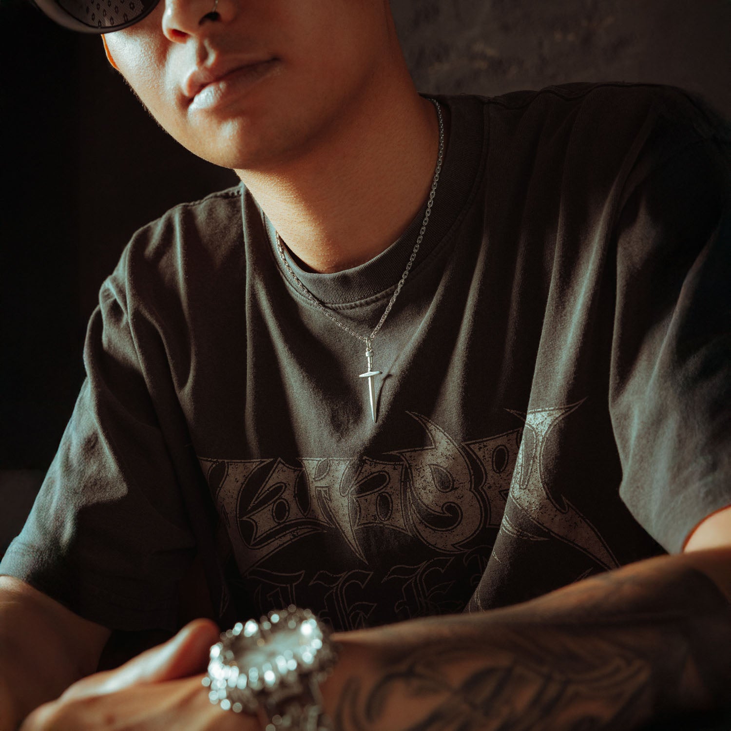 Silver chain with a dagger pendant on it, engraved with "Statement" on male model in grey shirt