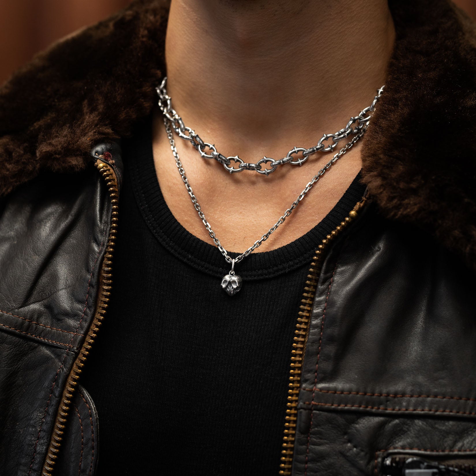 Man wearing a black leather jacket with fur collar and layered sterling silver necklaces by statement collective