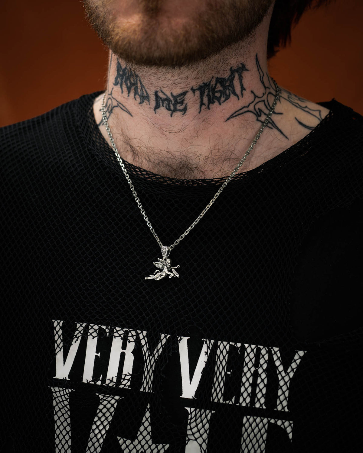 man with neck tattoo wearing sterling silver cherub pendant against dark orange background by statement collective