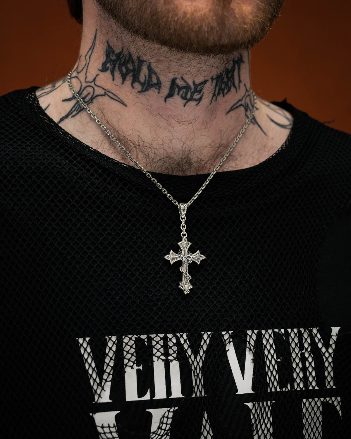 A person wearing the Statement Collective 925 Sterling Silver Mini “The Ruins” Cross Pendant and a black mesh shirt with bold white text. Visible tattoos adorn their neck, while only the lower half of their face is shown, emphasizing the striking gothic jewelry style.