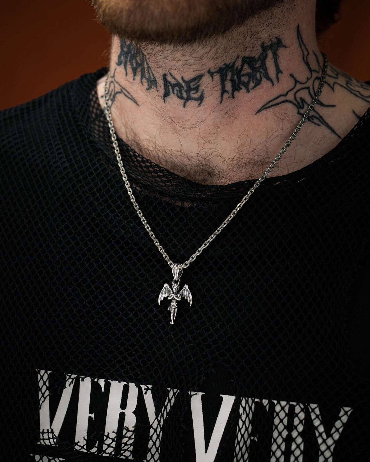 tattooed model wearing 925 silver cherub pendant with devil wings against orange background