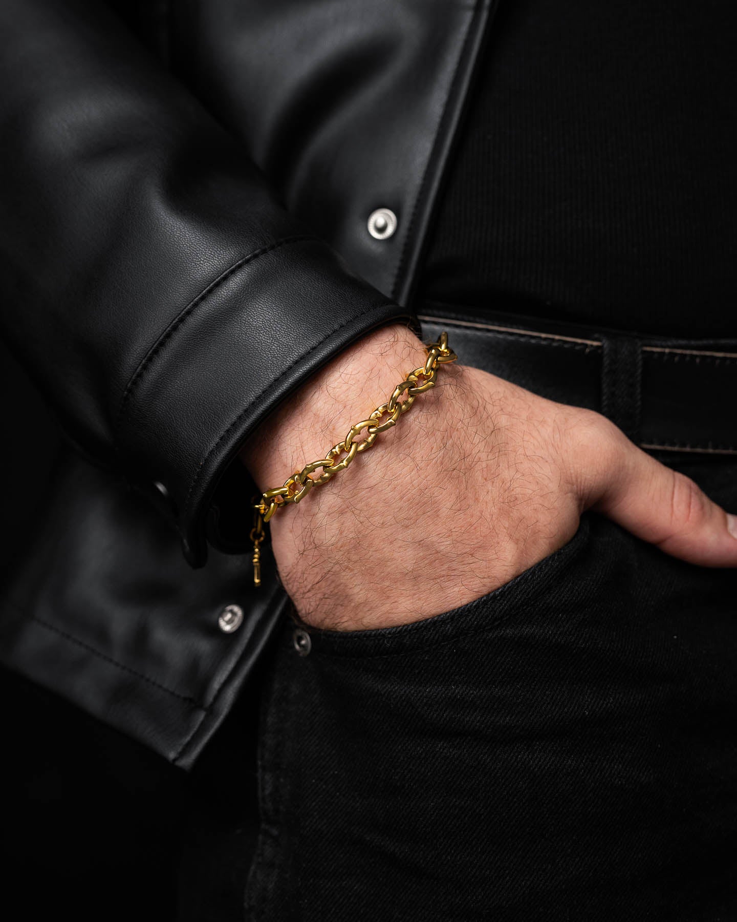 A person wearing "The Cathedral" 9mm Spiked Bracelet (Gold) and a black leather jacket has their hand in the pocket of black jeans, set against a dark background.