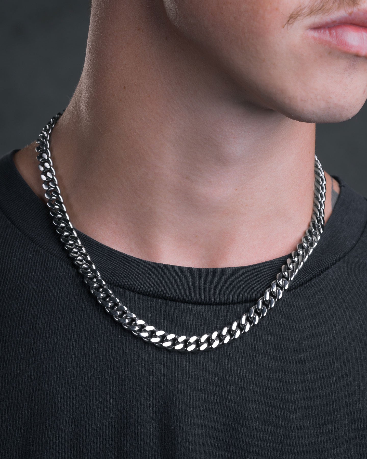 A close-up shows a person in a black shirt wearing the shiny 9mm Cuban Chain choker, focusing on their lower face, neck, collarbone, and a partial mustache.
