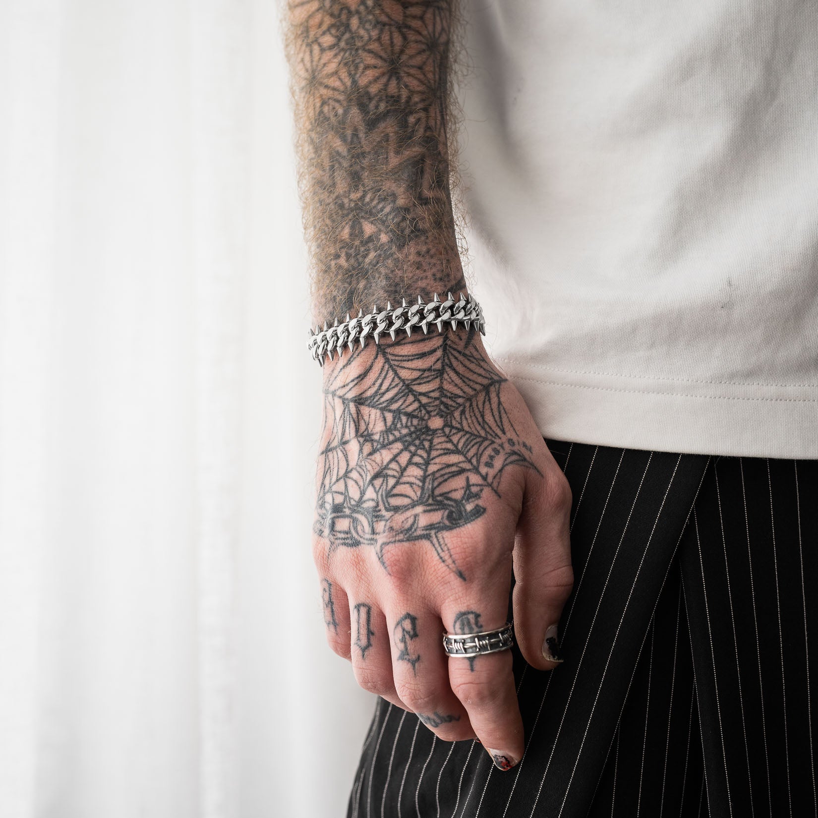 Person with tattooed hand wearing a silver spiked cuban chain bracelet on a white background