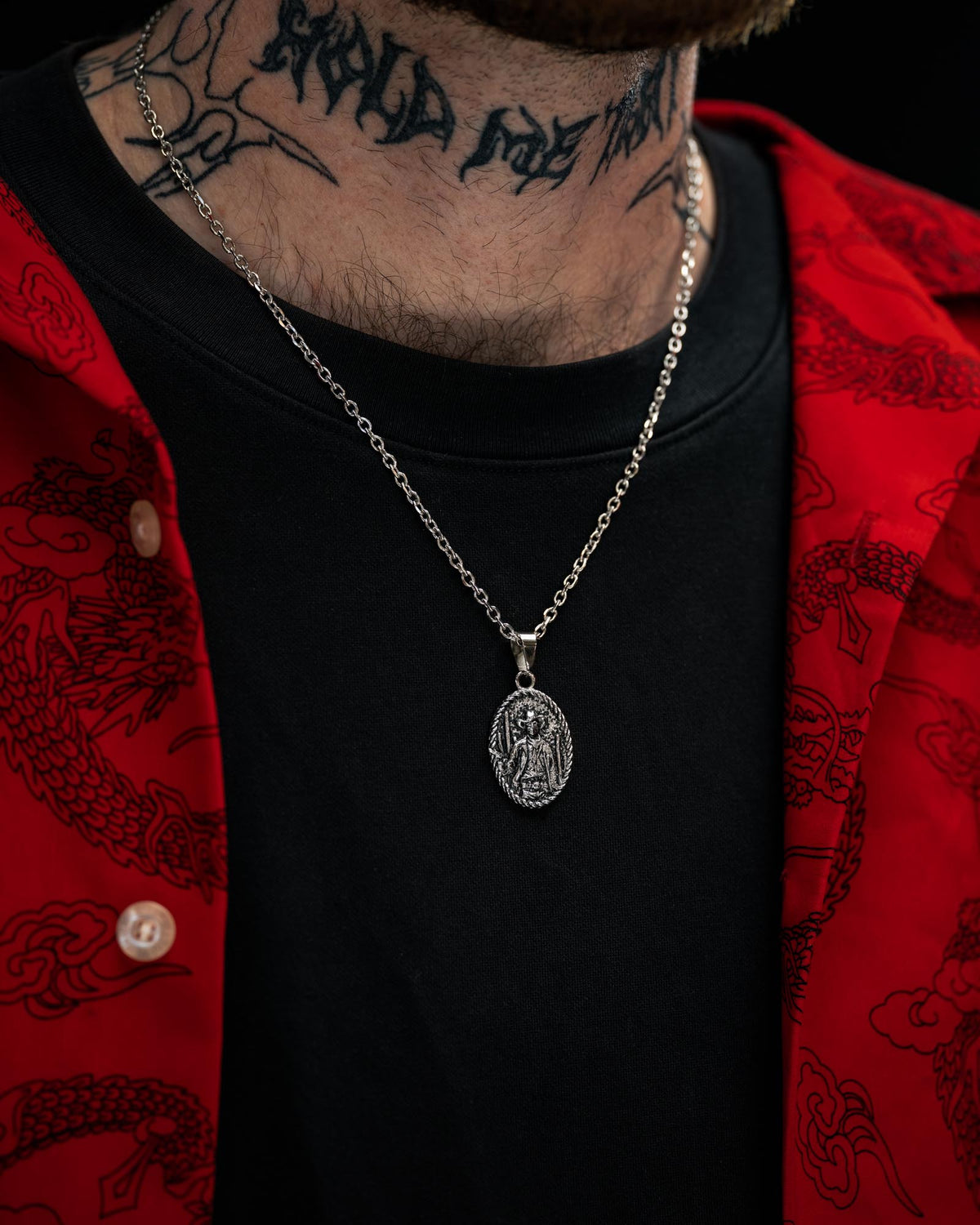 A person wearing a red patterned shirt over a black t-shirt, accessorized with STATEMENT’s “Big Iron” Pendant necklace and black script tattoo on their neck.