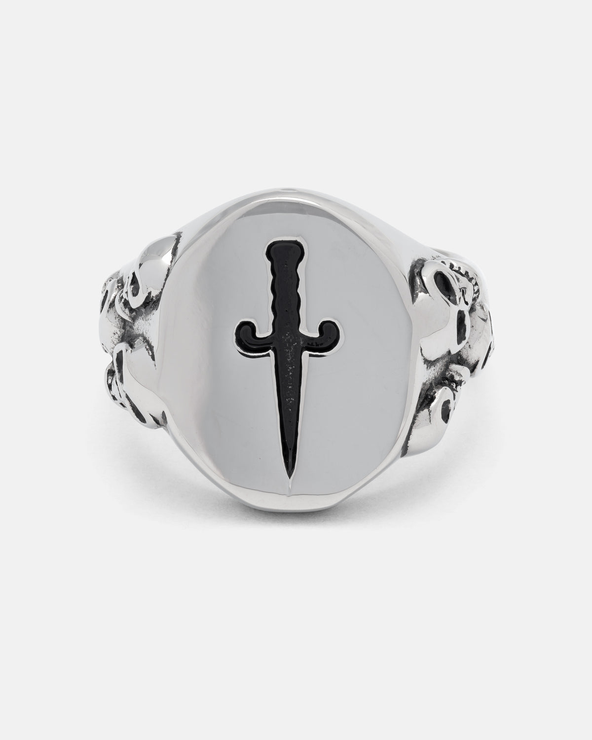 The Graveyard Signet Ring by Statement Collective commands attention with its bold stainless steel design, showcasing an engraved black dagger on its circular face and intricate skull details along each side of the band—all set off dramatically against a plain white background.