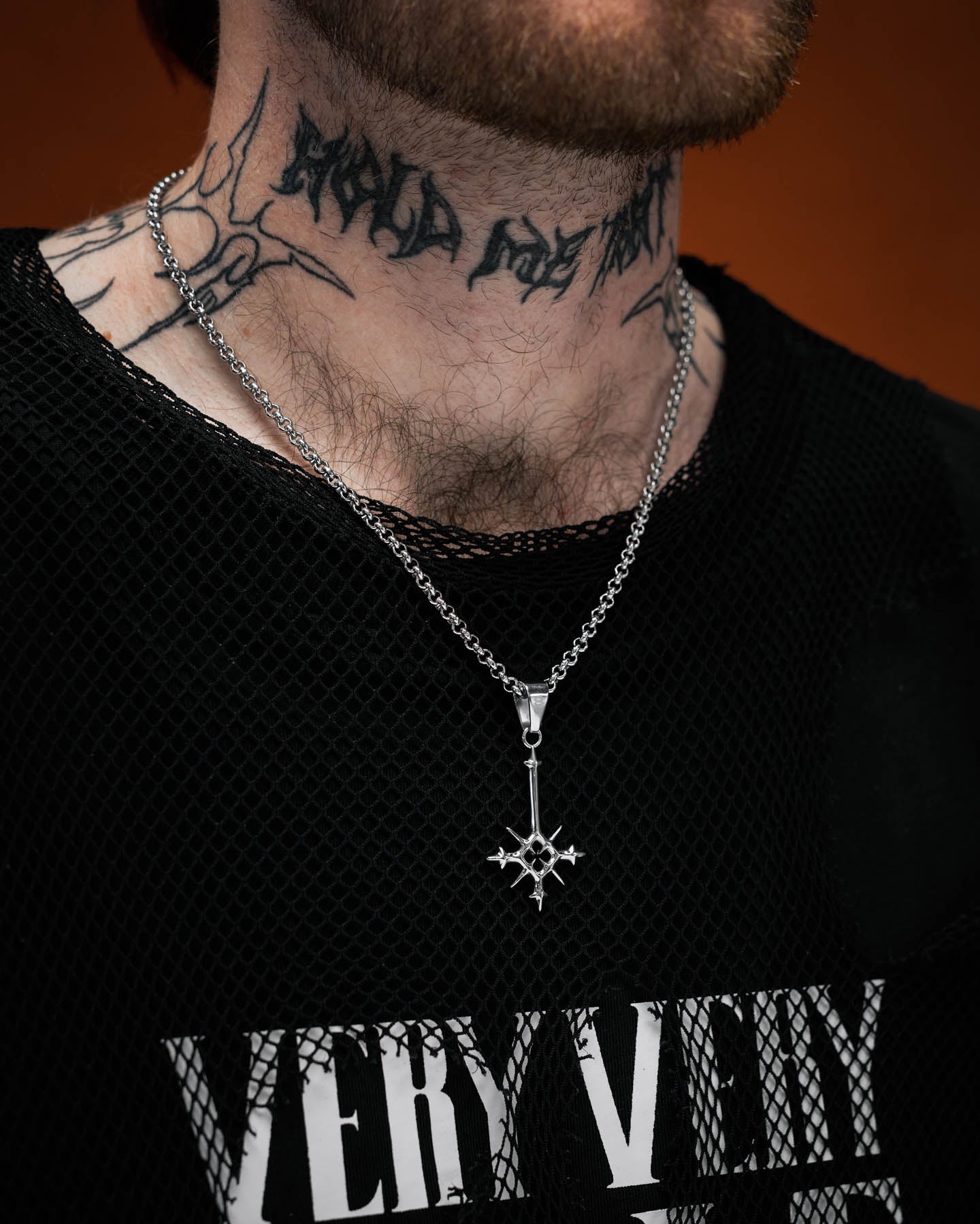 tattooed model wearing small size spiked cross pendant against orange background