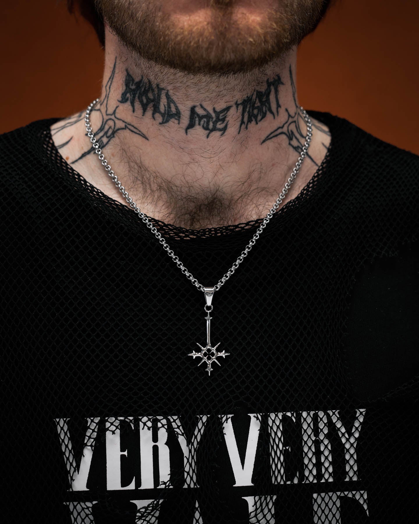 tattooed model wearing small size spiked cross pendant against orange background by statement collective