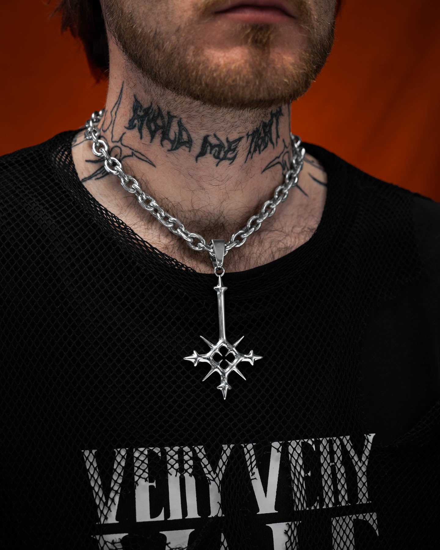 Person wearing a black shirt with visible text and a silver necklace with a star pendant against an orange background.