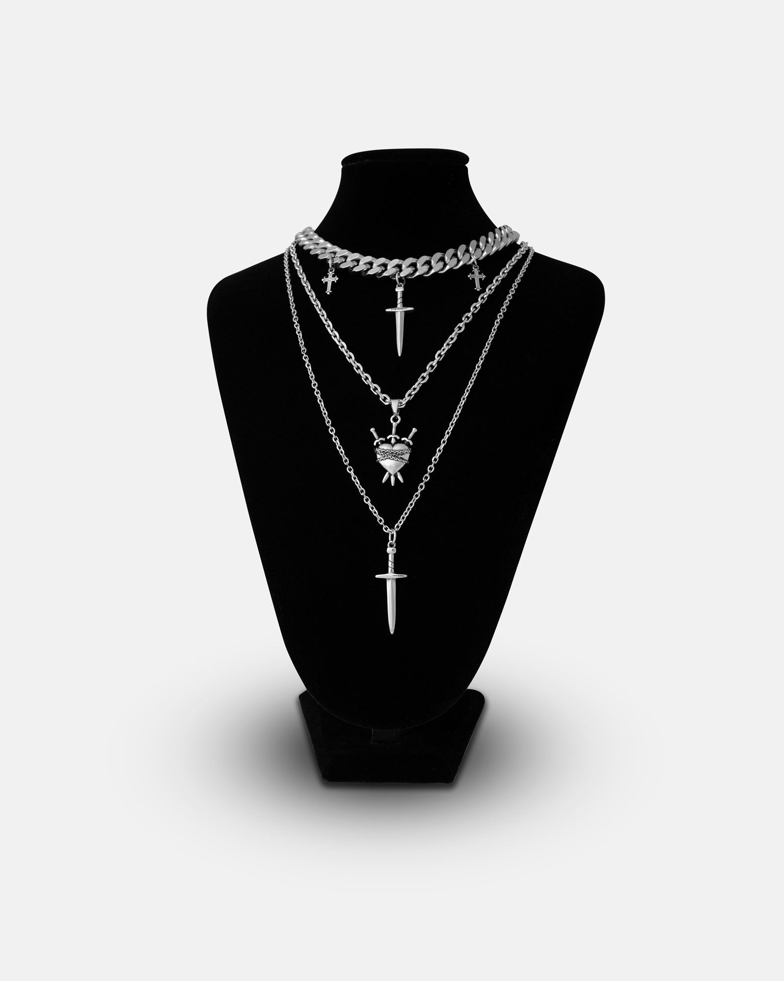 The Tough Love Stack features four silver chain necklaces, each with a matching dagger pendant, styled on a black bust. The chains vary in length and thickness for an edgy, bold grunge look against a white background.